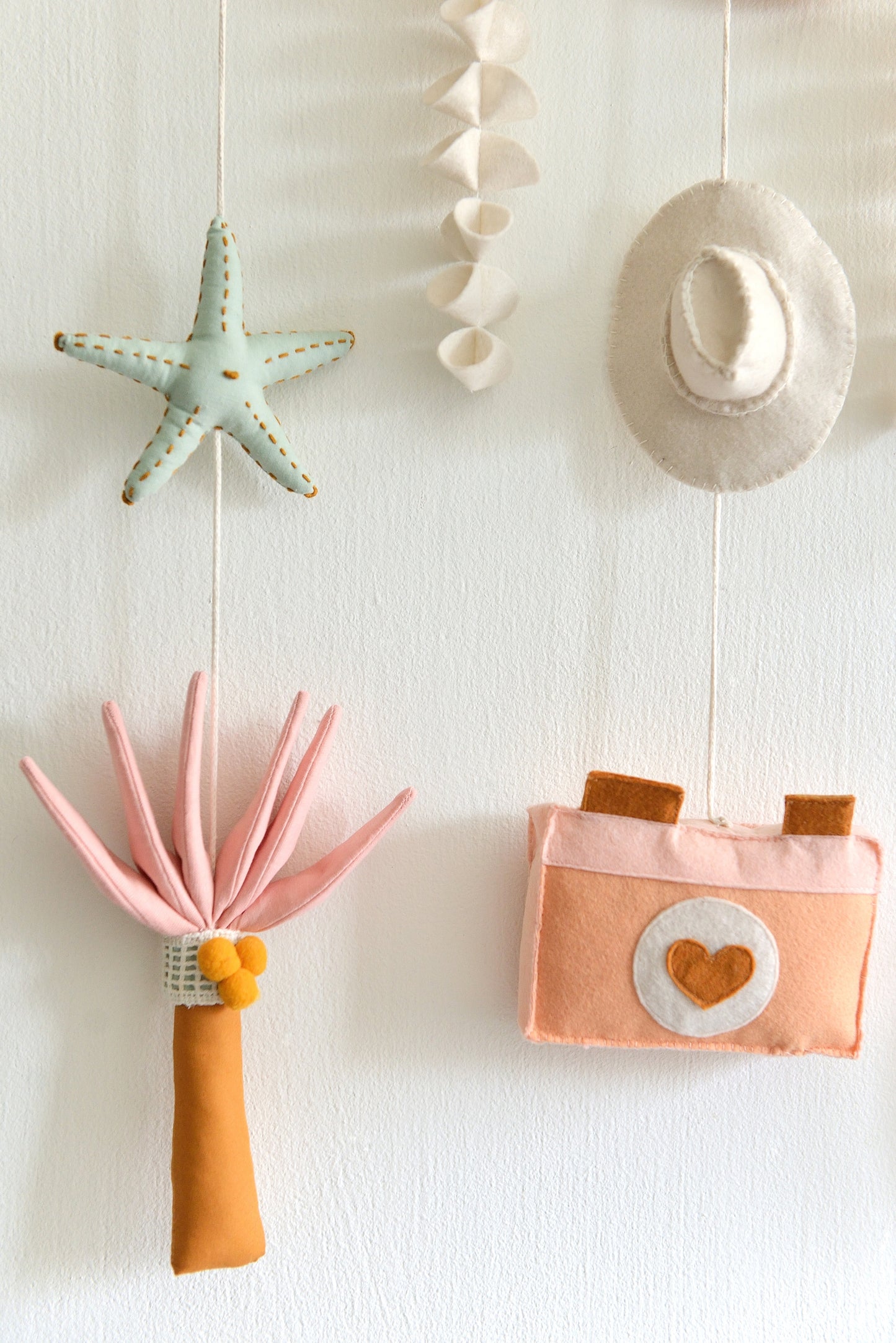 Decorative wall hanging with various coastal figures including a cowboy hat, starfish, palm and camera against a light wall.