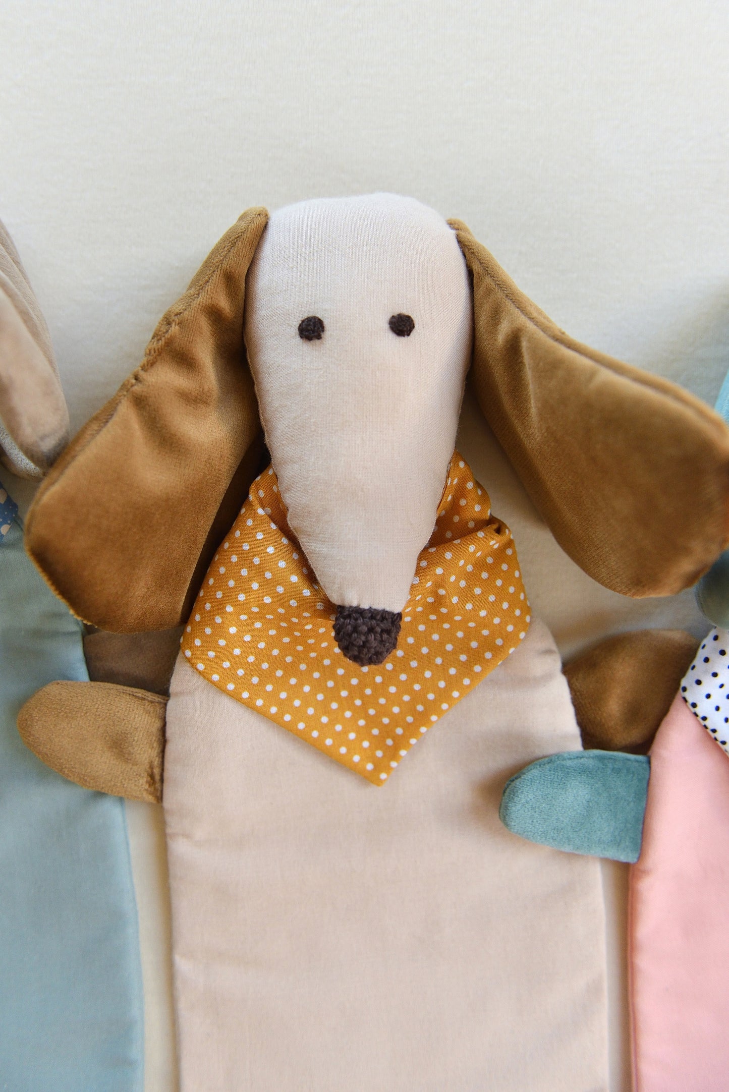 Dachshund Comforter up close with long ears and snouts featuring a cream body and brown coloured shiny ears. It wears an ochre bandana with white dots conveying a playful and cozy feel.