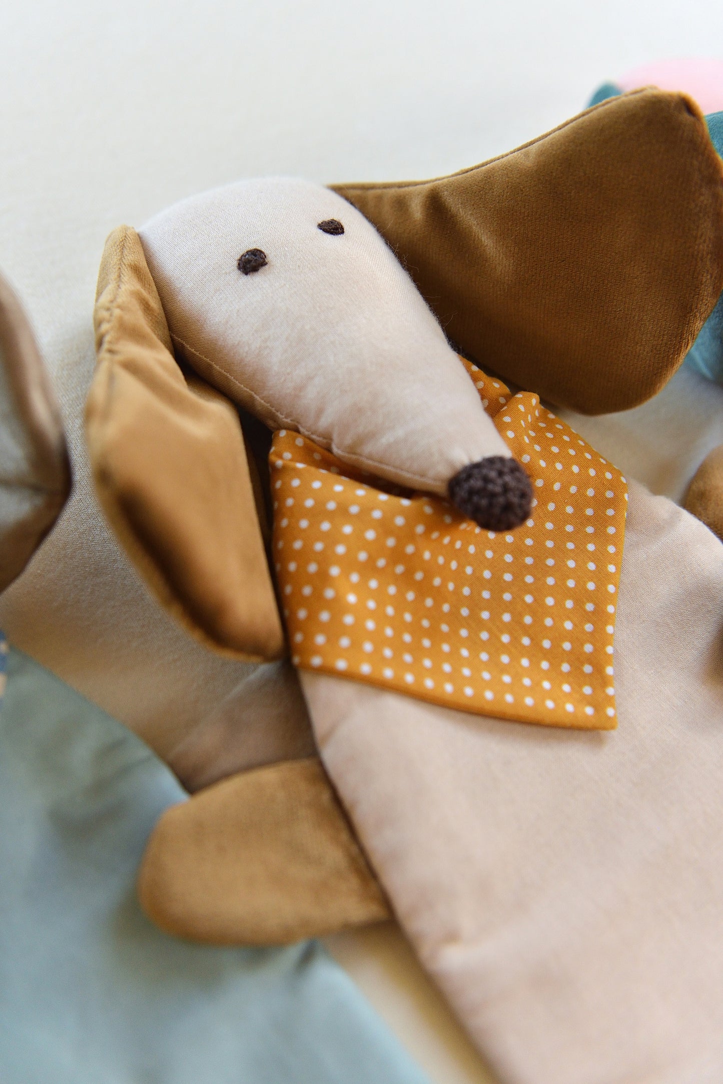 Dachshund Comforter from the side with long ears and snouts featuring a cream body and brown coloured shiny ears. It wears an ochre bandana with white dots conveying a playful and cozy feel.