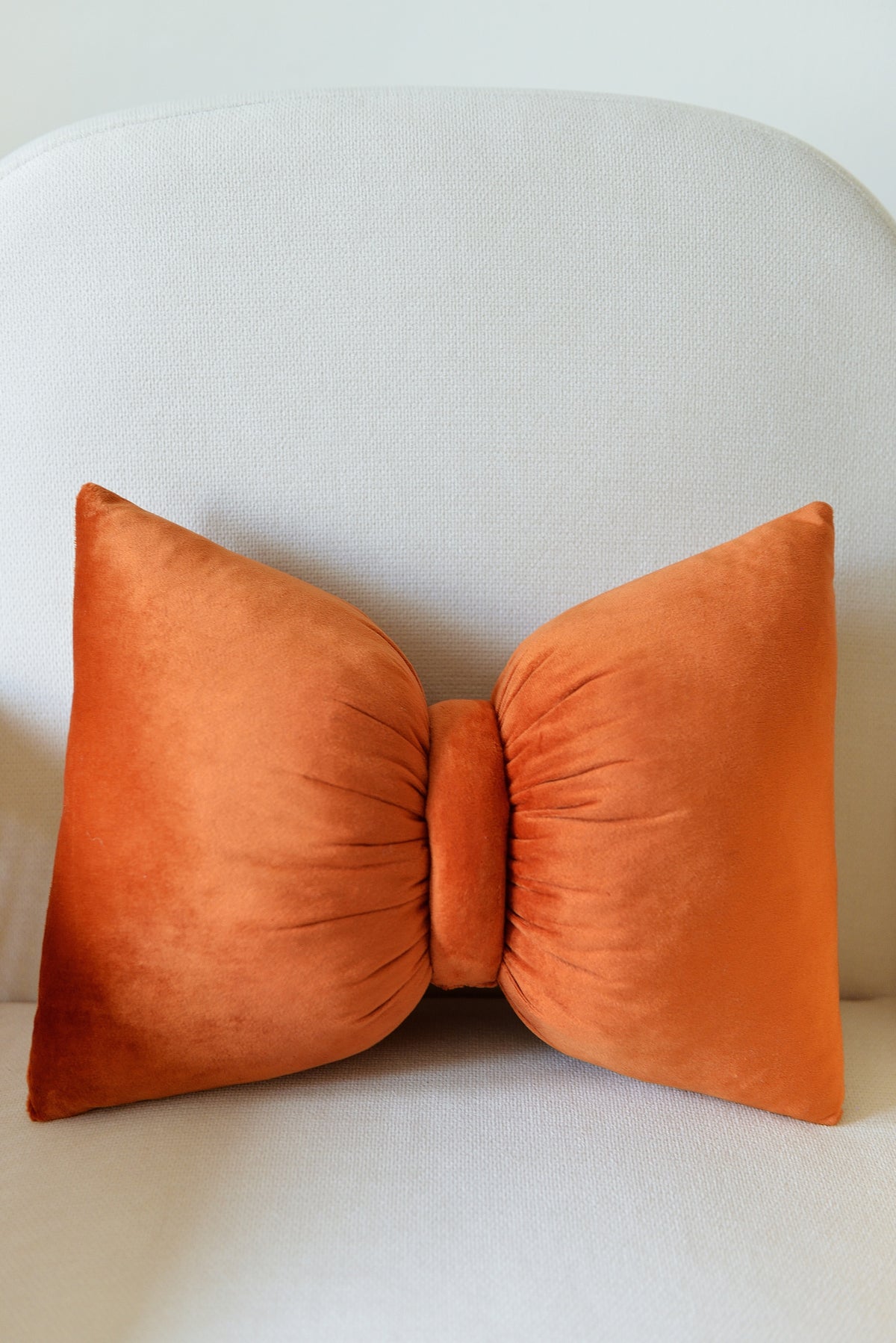 Rust velvet bow pillow on an ivory armchair.