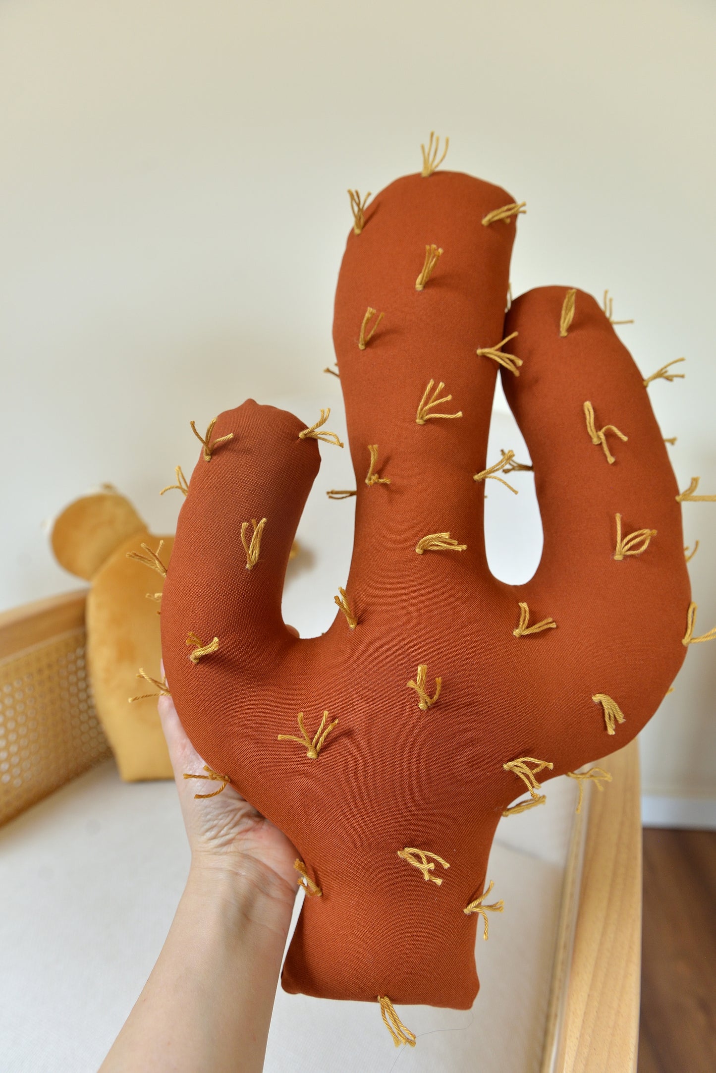 Hand holding a terracotta-colored cactus-shaped decor pillow against a neutral background.