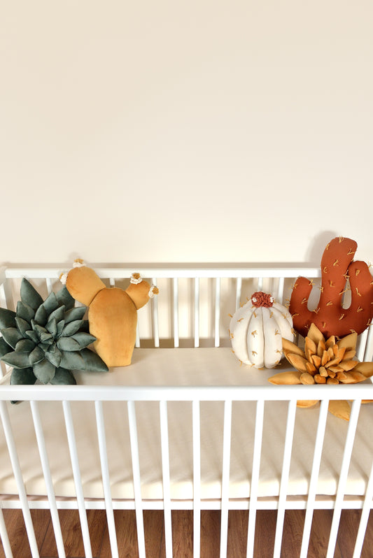 Set of cactus-shaped decor pillows in various colors in a white baby crib.