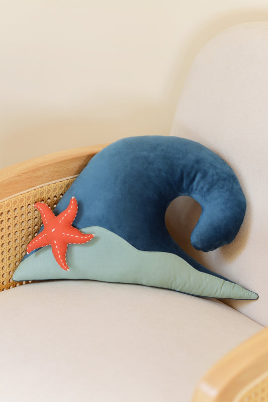 Ocean Blue wave shaped decor pillow with dark mint green sandy base and coral red starfish on an ivory rattan armchair.
