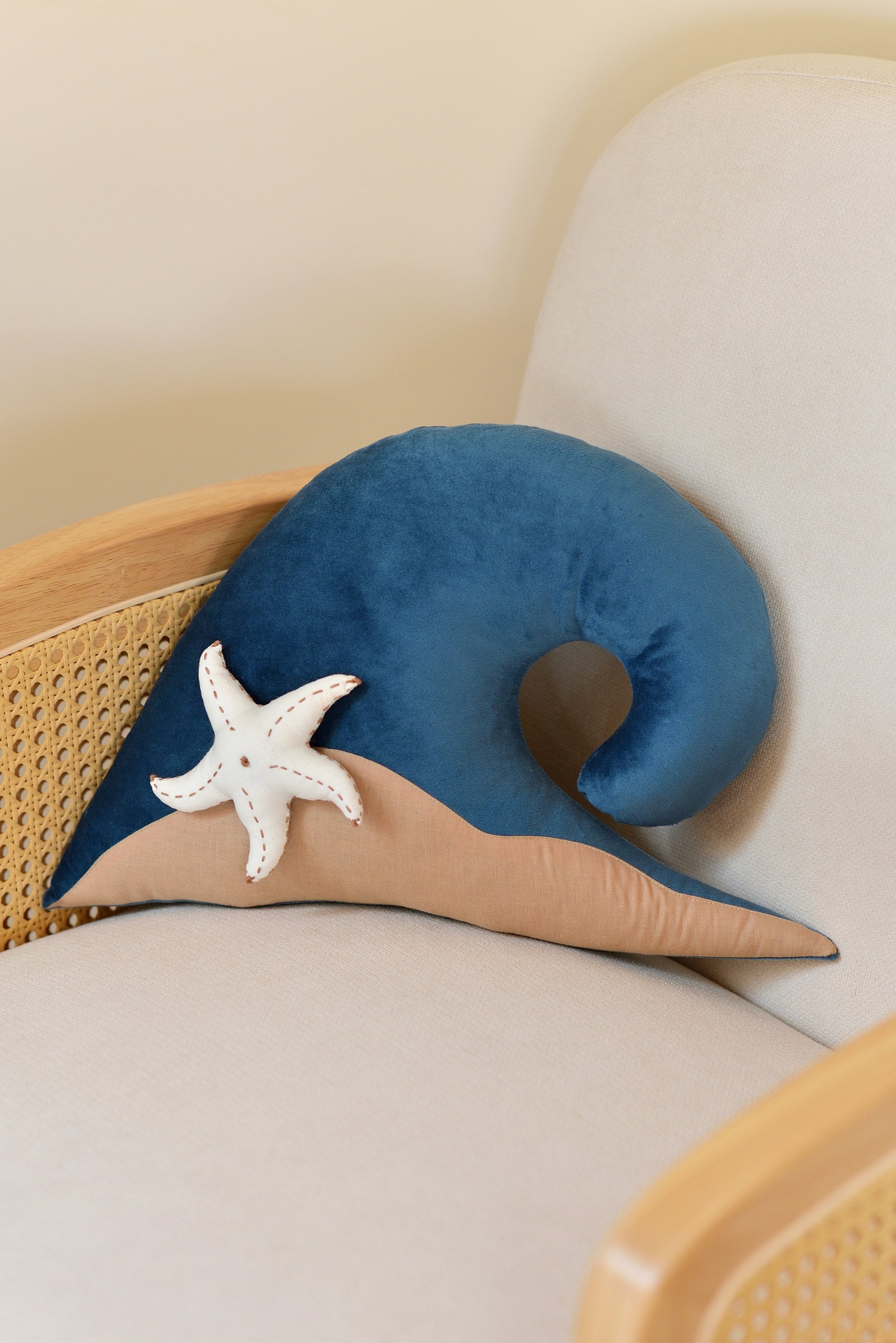 Ocean Blue wave shaped decor pillow with tan sandy base and white starfish on an ivory rattan armchair.