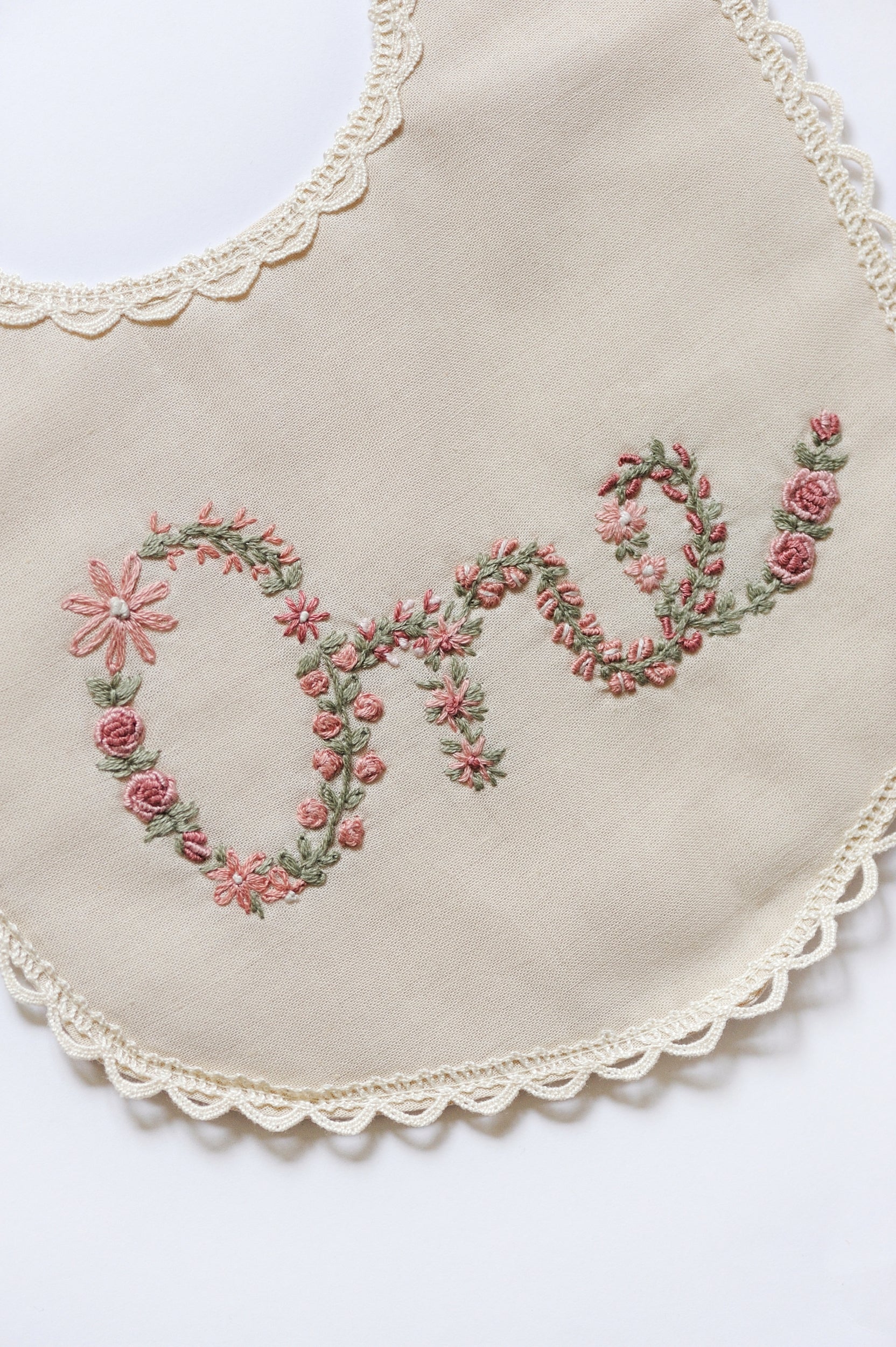 Embroidered floral design spelling ONE on an ivory bib with lace trim