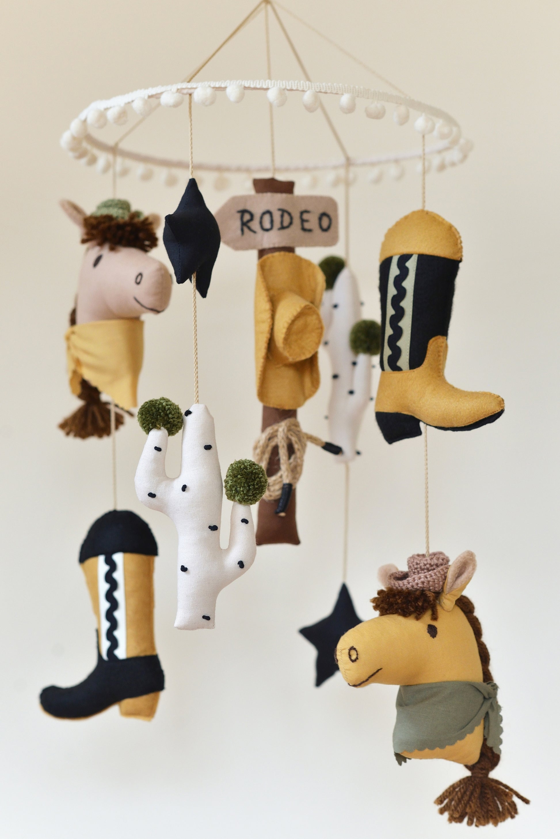 Handmade Wild West rodeo nursery mobile with cowboy boots, hats, horses, cacti, stars, and rodeo signpost in boho desert style.