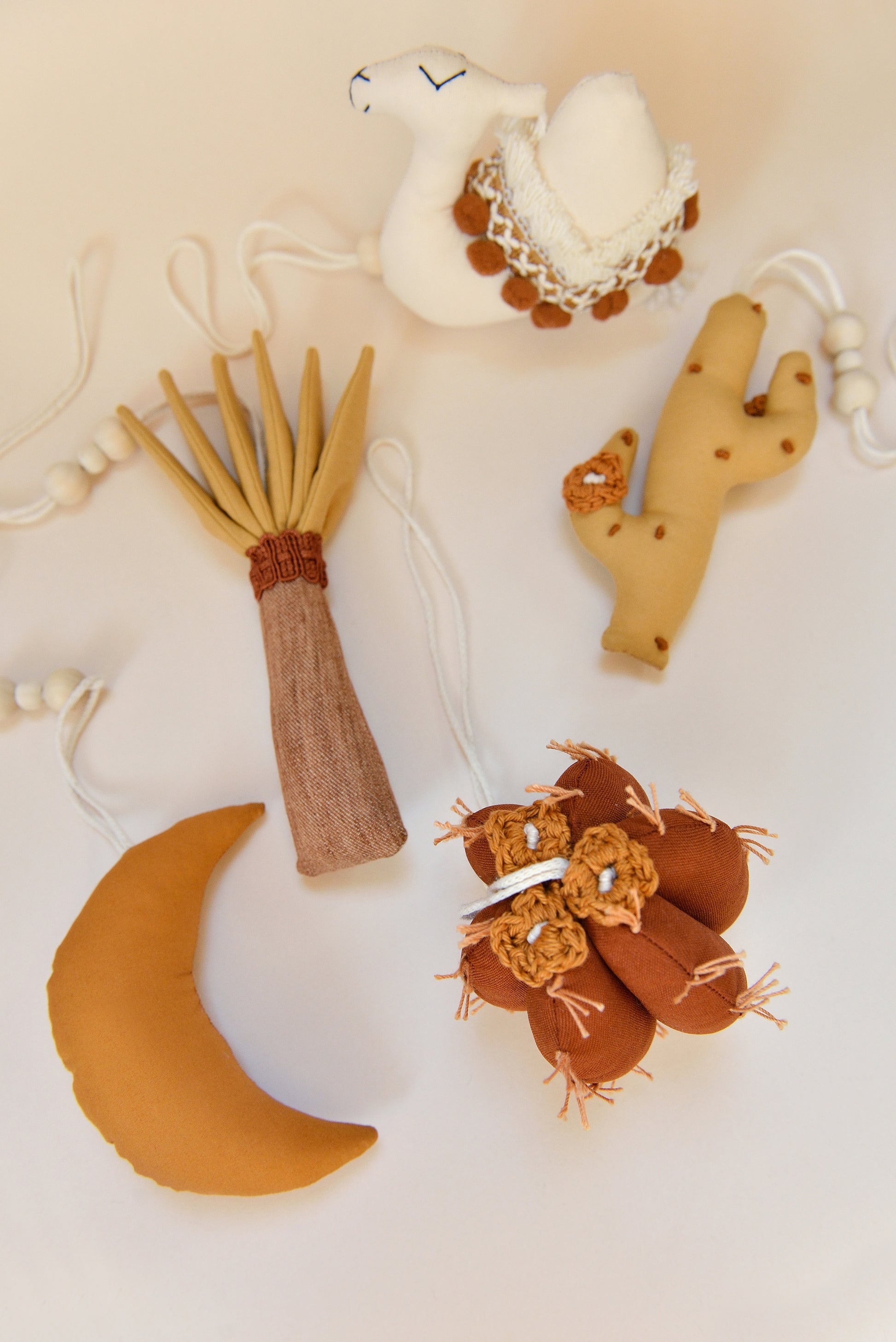 Flatlay of desert themed earthy colour baby play gym toys on an ivory background: palm, moon, cacti, camel.