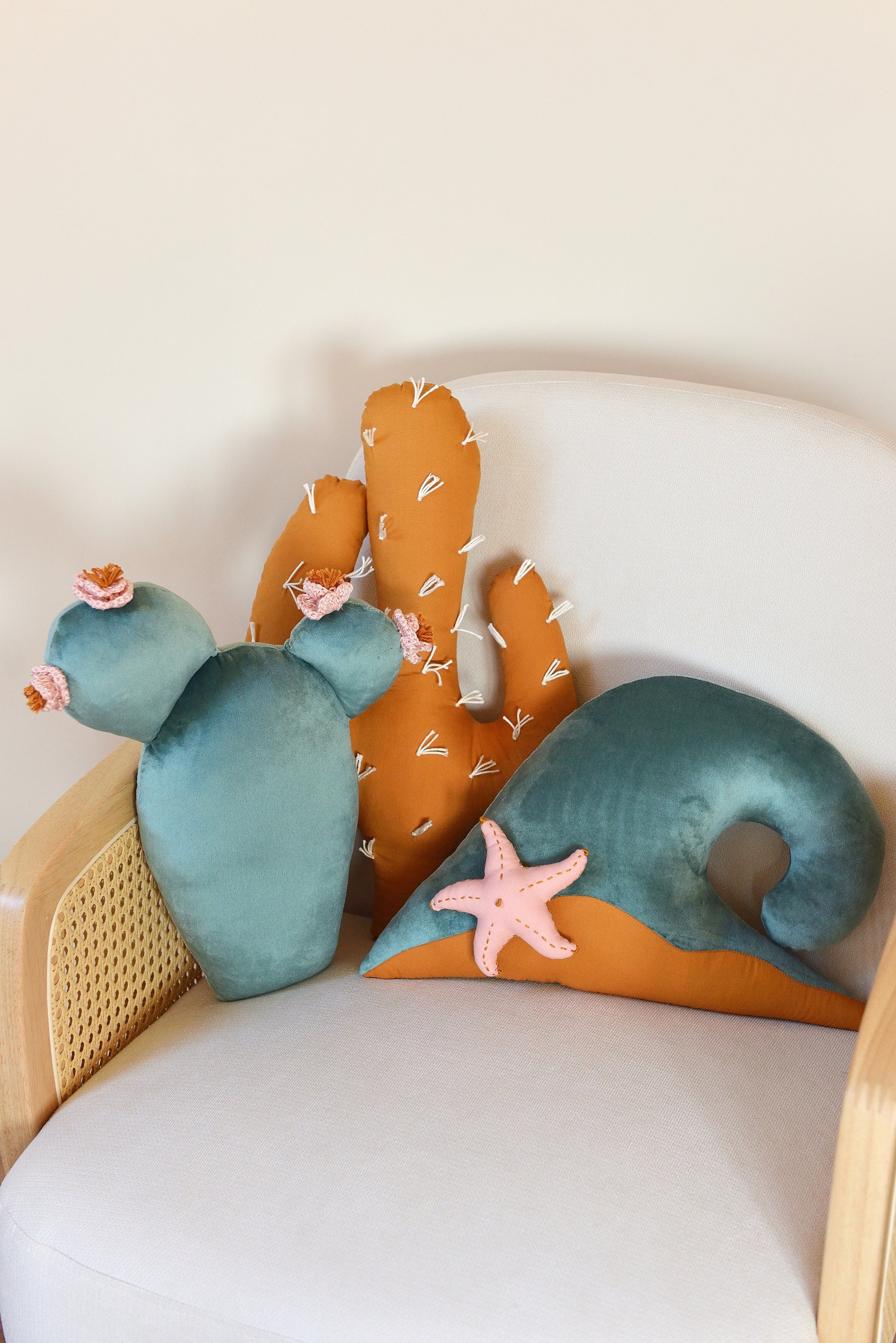 Prickly pear, saguaro cactus and ocean wave shaped decor pillow placed on an ivory armchair.