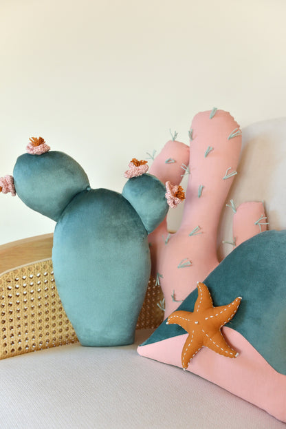 Prickly pear, saguaro cactus and ocean wave shaped decor pillow placed on an ivory armchair.