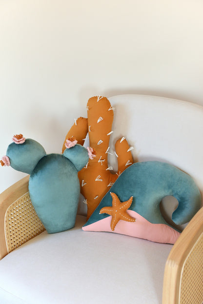 Prickly pear, saguaro cactus and ocean wave shaped decor pillow placed on an ivory armchair.