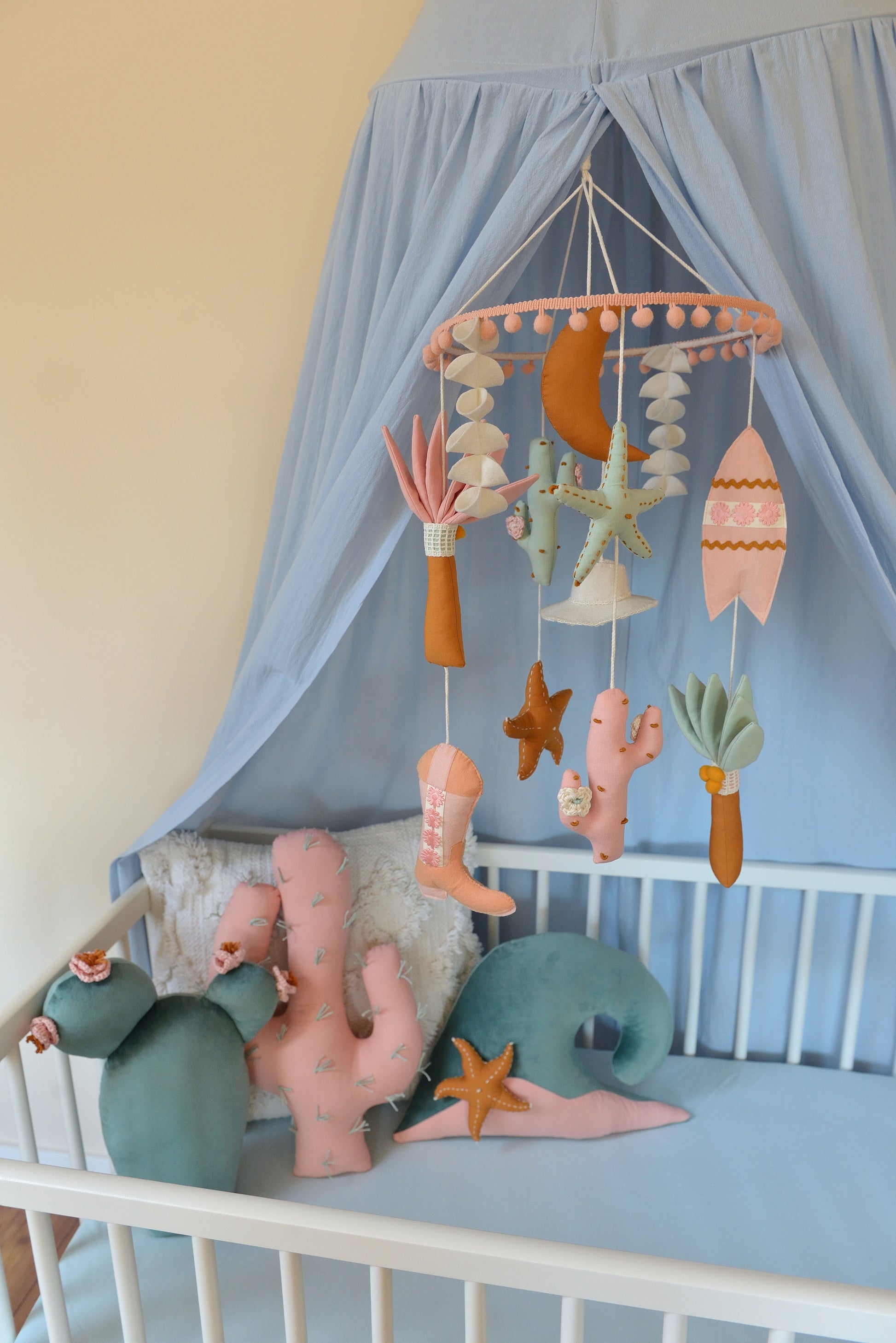 Baby crib with canopy, decorative pillows and a mobile hanging above.