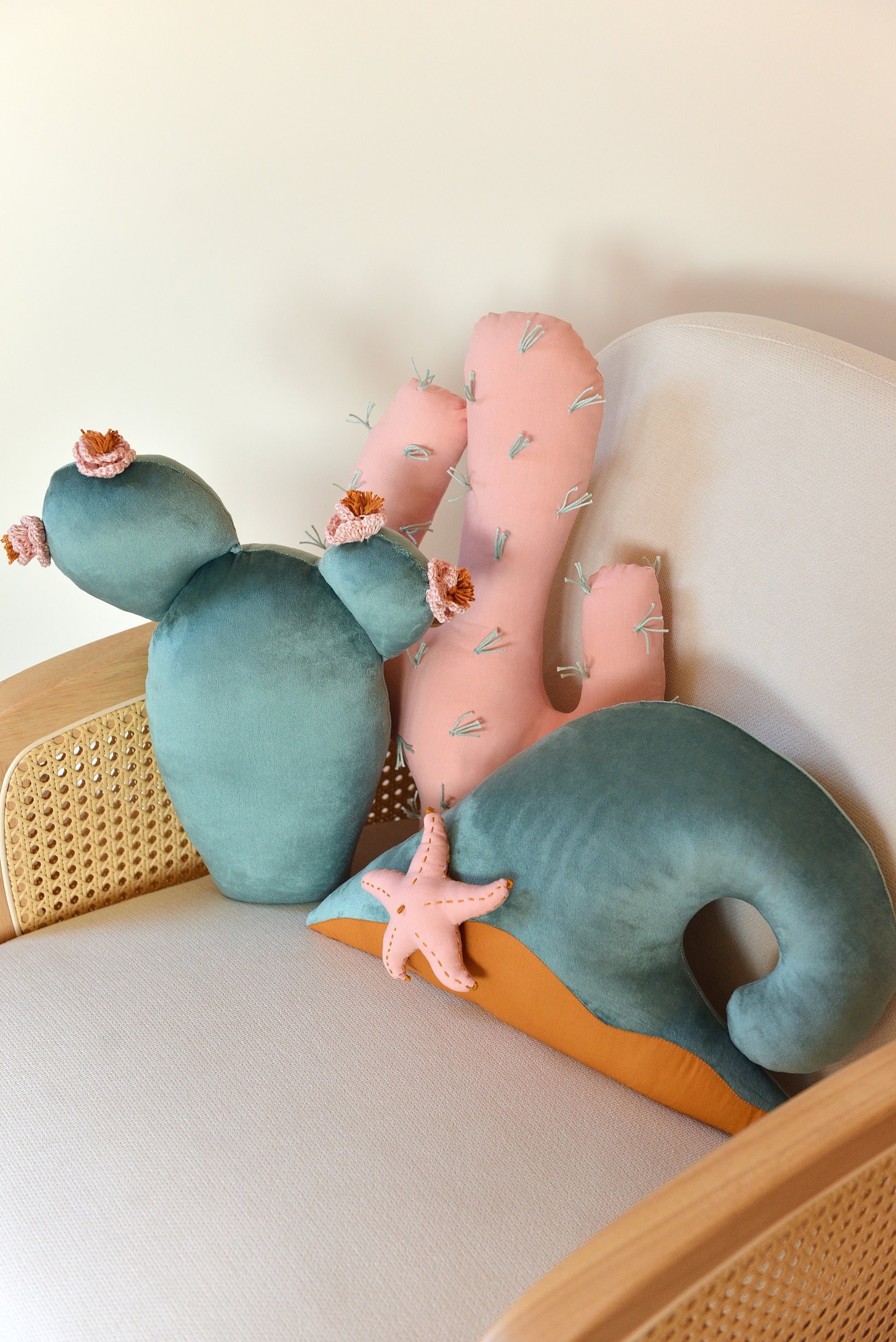 Prickly pear, saguaro cactus and ocean wave shaped decor pillow placed on an ivory armchair.