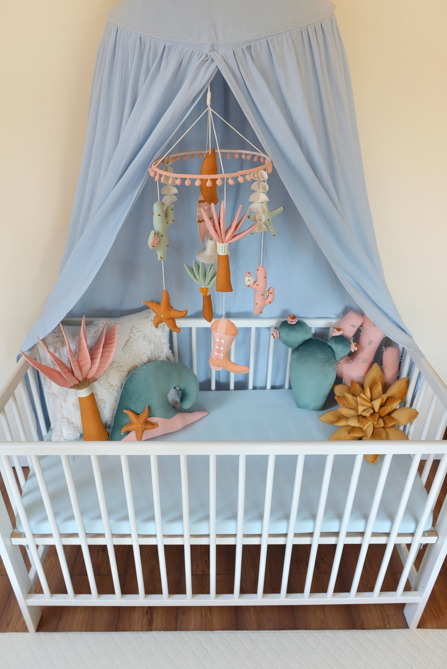Baby crib with canopy, decorative pillows and a mobile hanging above.