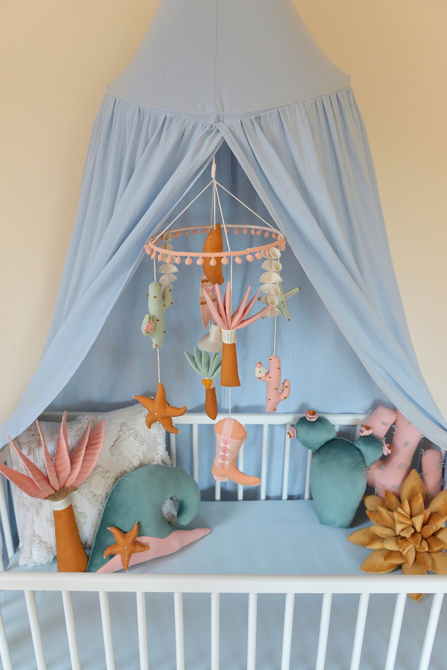 Baby crib with canopy, decorative pillows and a mobile hanging above.