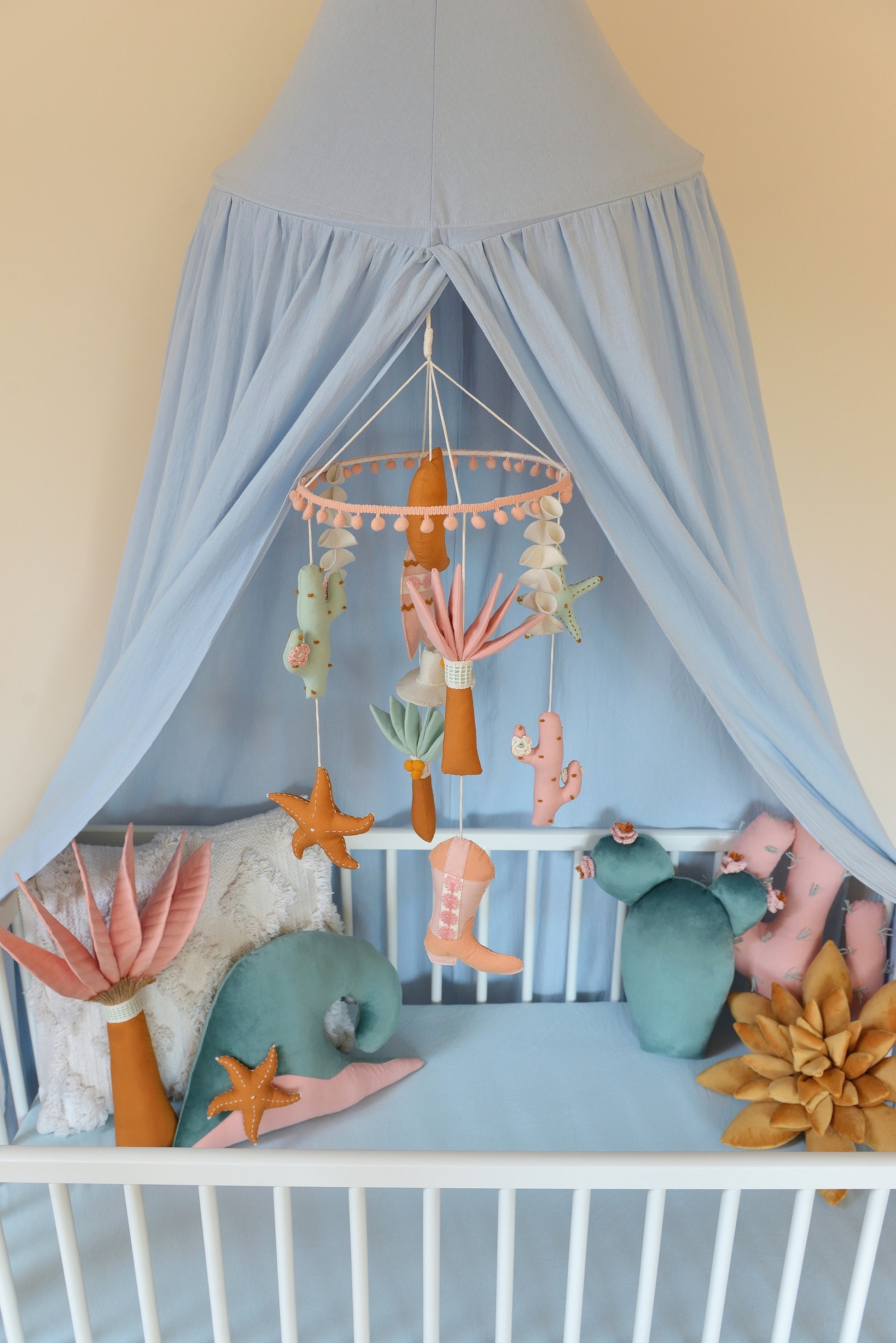 Baby crib with canopy, decorative pillows and a mobile hanging above.