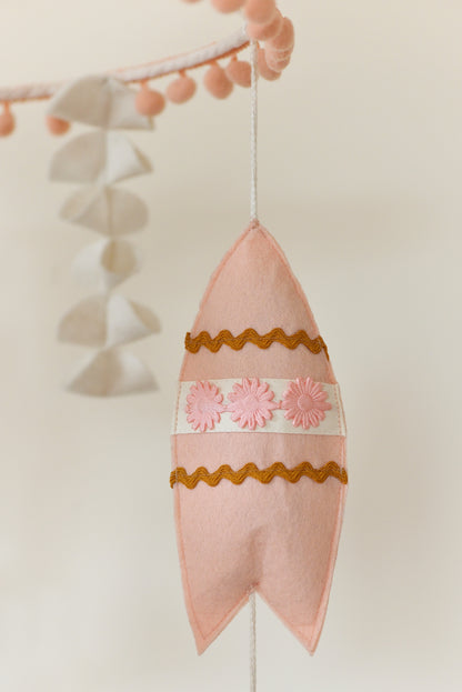 Peachy pink surf board hanging off a nursery mobile hoop.