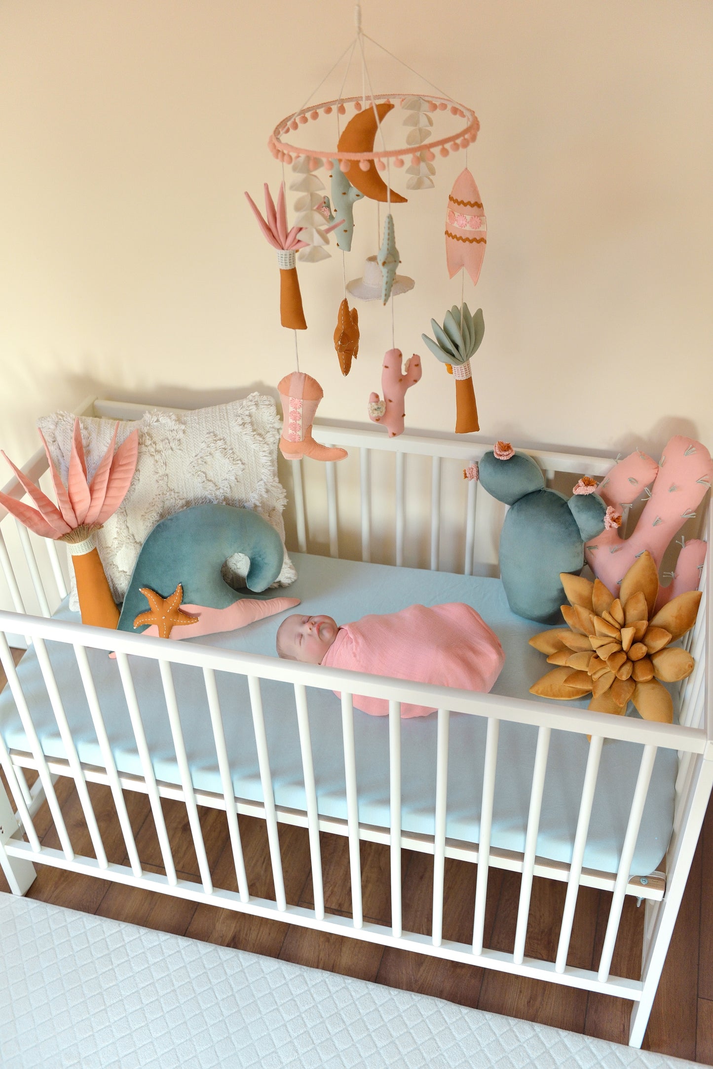 Baby crib with baby, decorative pillows and a mobile hanging above.