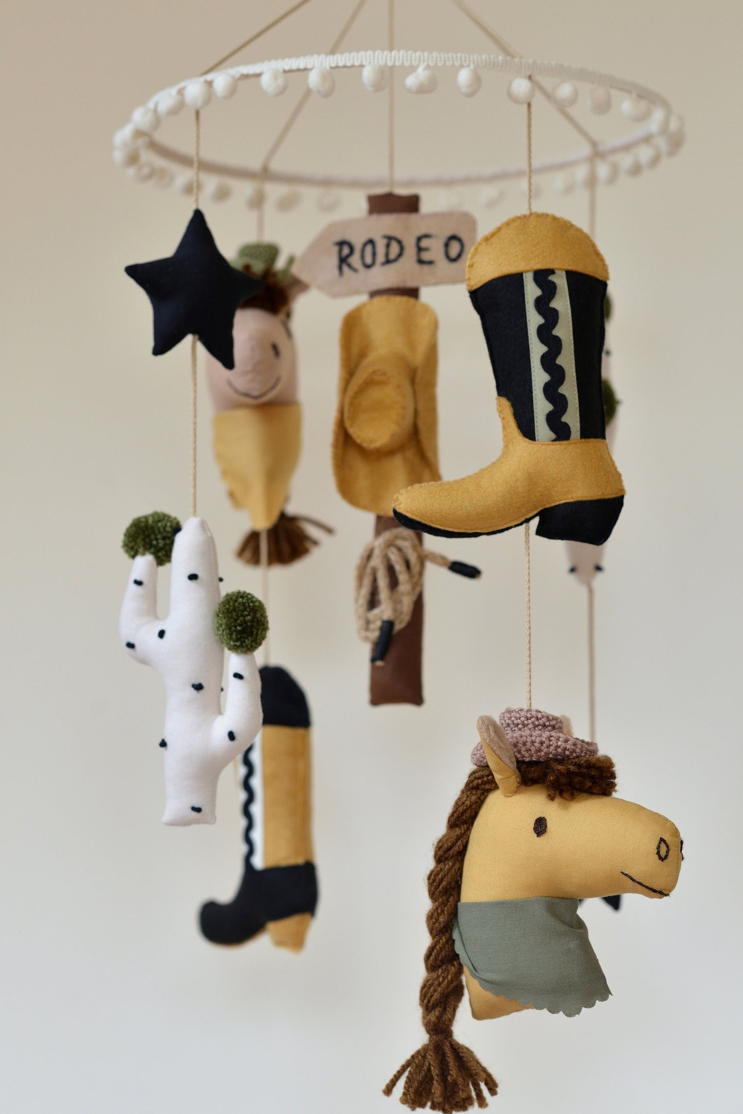 Handmade Wild West rodeo nursery mobile with cowboy boots, hats, horses, cacti, stars, and rodeo signpost in boho desert style.
