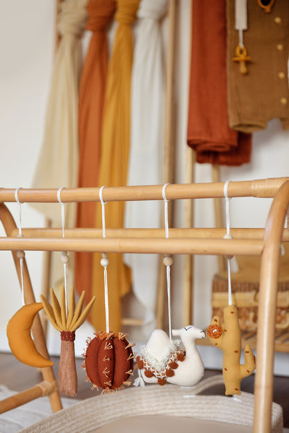 Desert themed earthy colour baby play gym toys hanging on a rattan gym stand: palm, moon, cacti, camel.