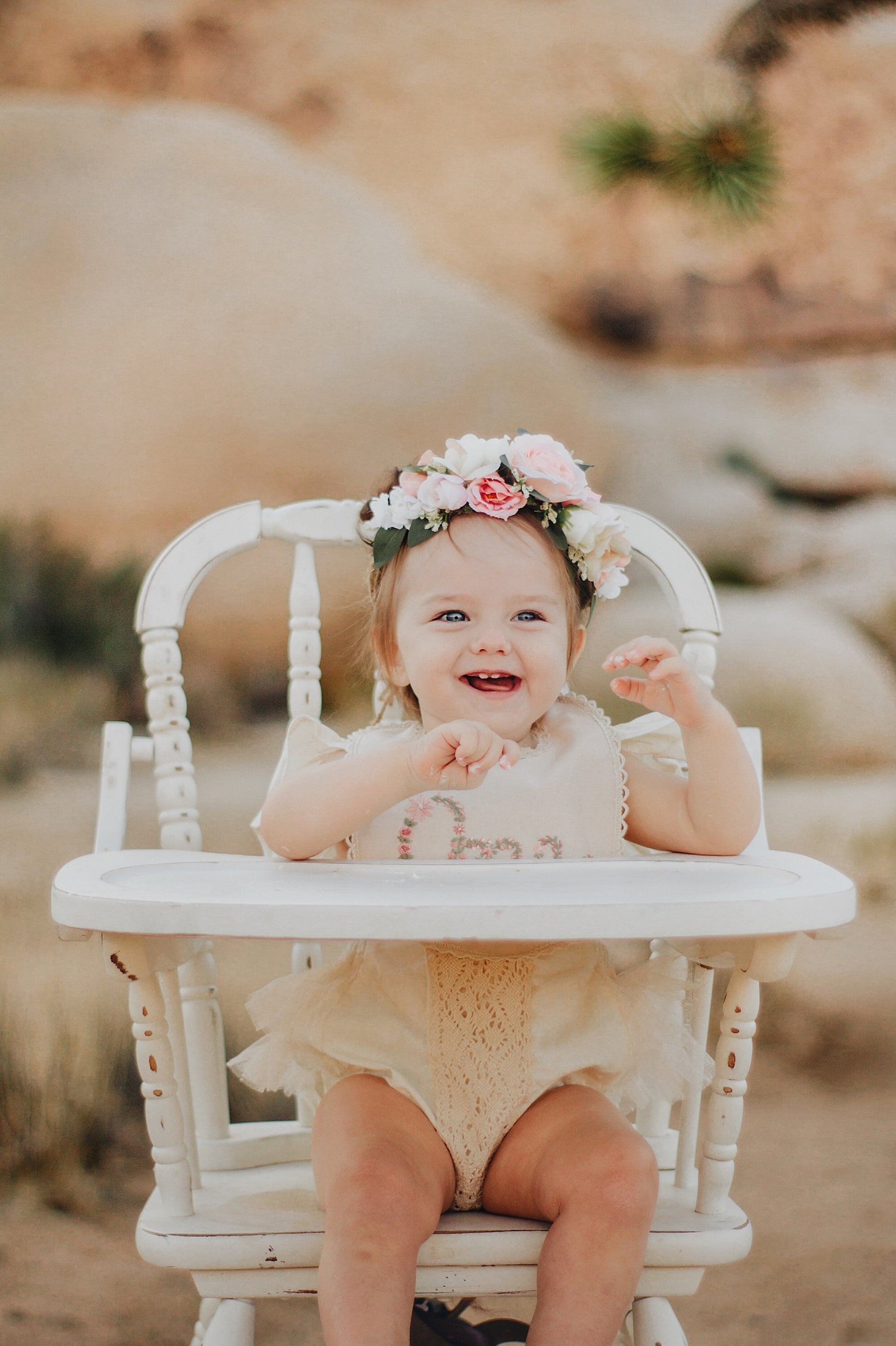 Baby sitting in a high chair with a floral cown wearing an embroidered bib in Joshua Tree