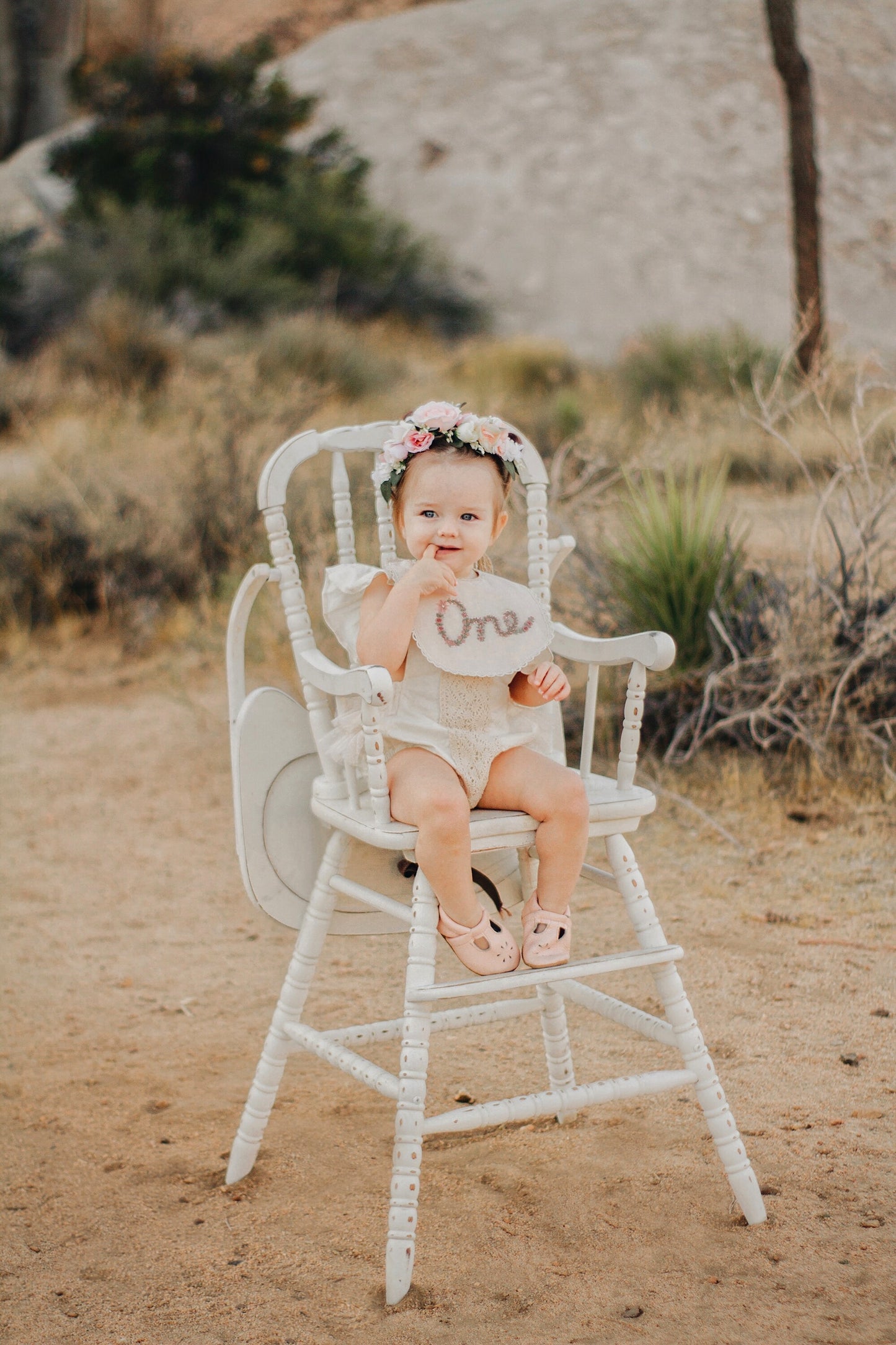 Baby sitting in a high chair with a floral cown wearing an embroidered bib in Joshua Tree