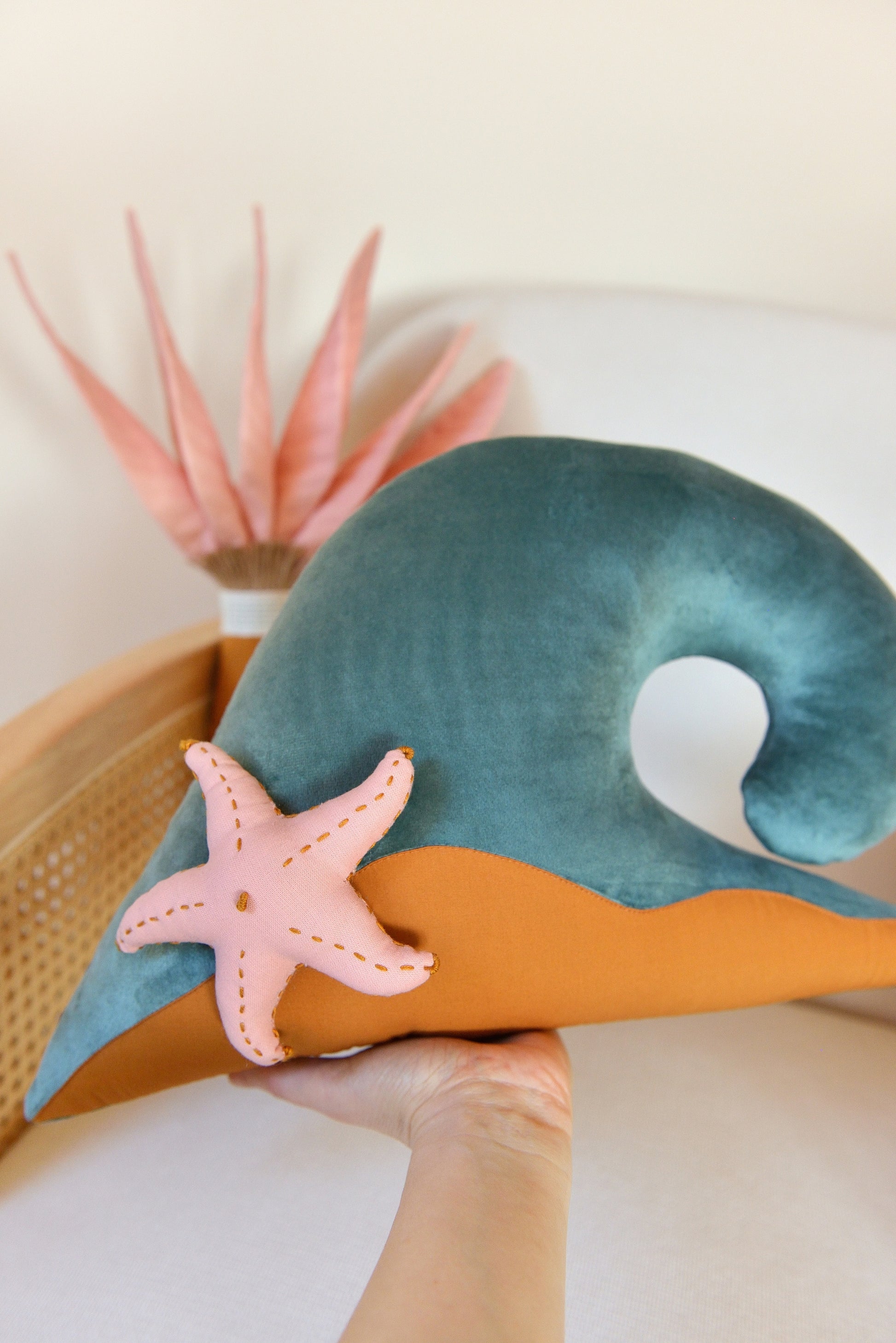 Hand holding an ocean wave shaped decor pillow accented with a starfish.