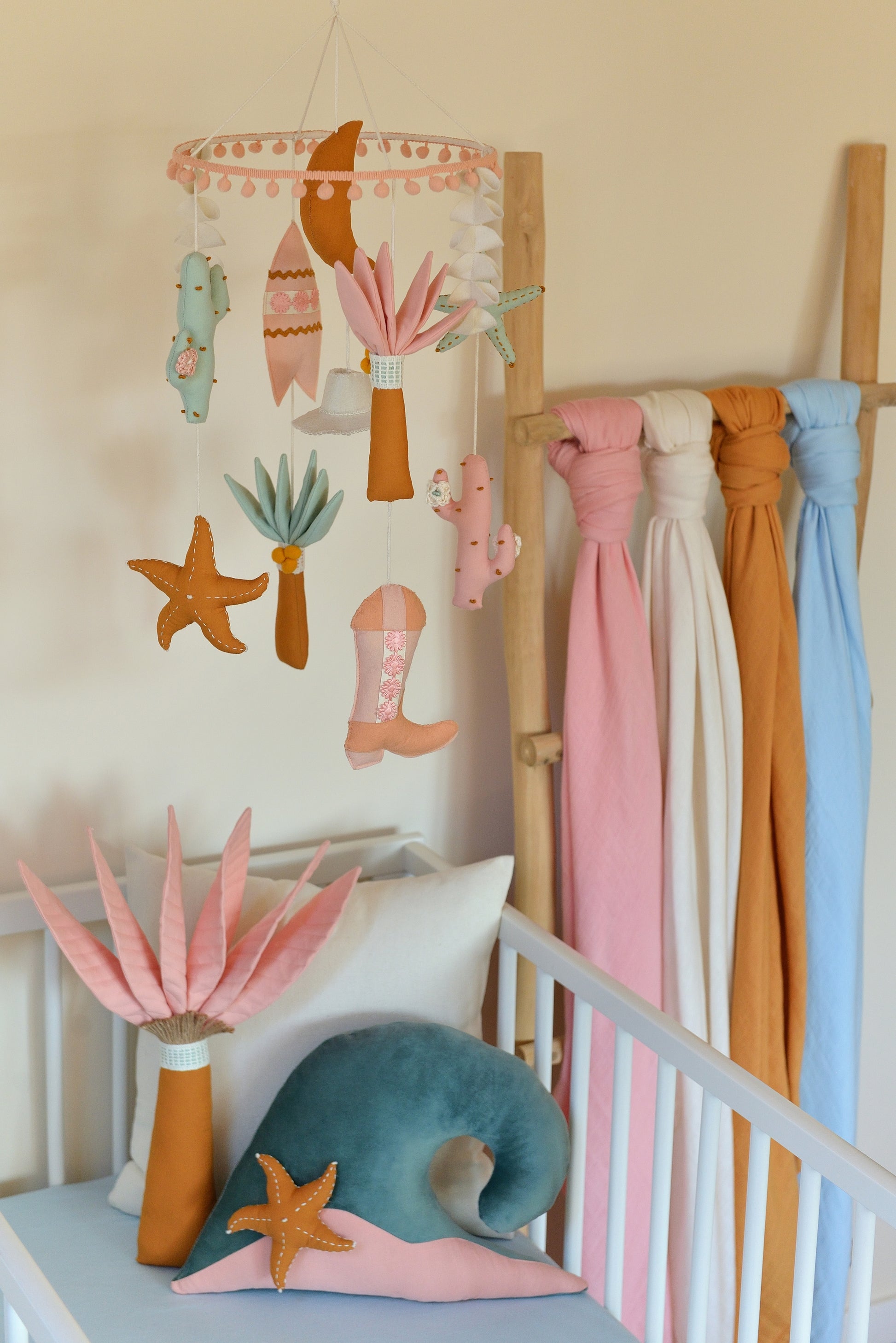 Surf themed baby room with crib, decorative pillows, nursery mobile and swaddles displayed on a ladder.