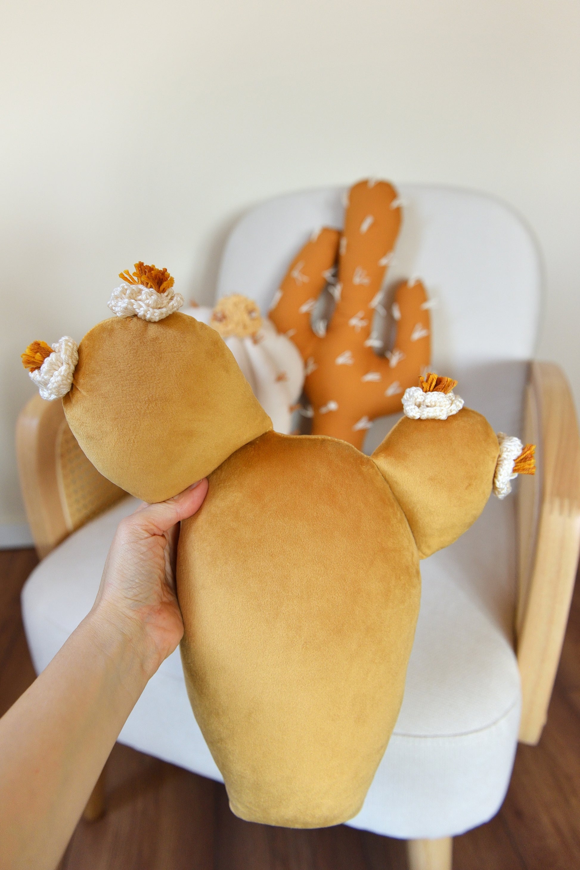 Hand holding gold prickly pear cactus shaped decor pillow.