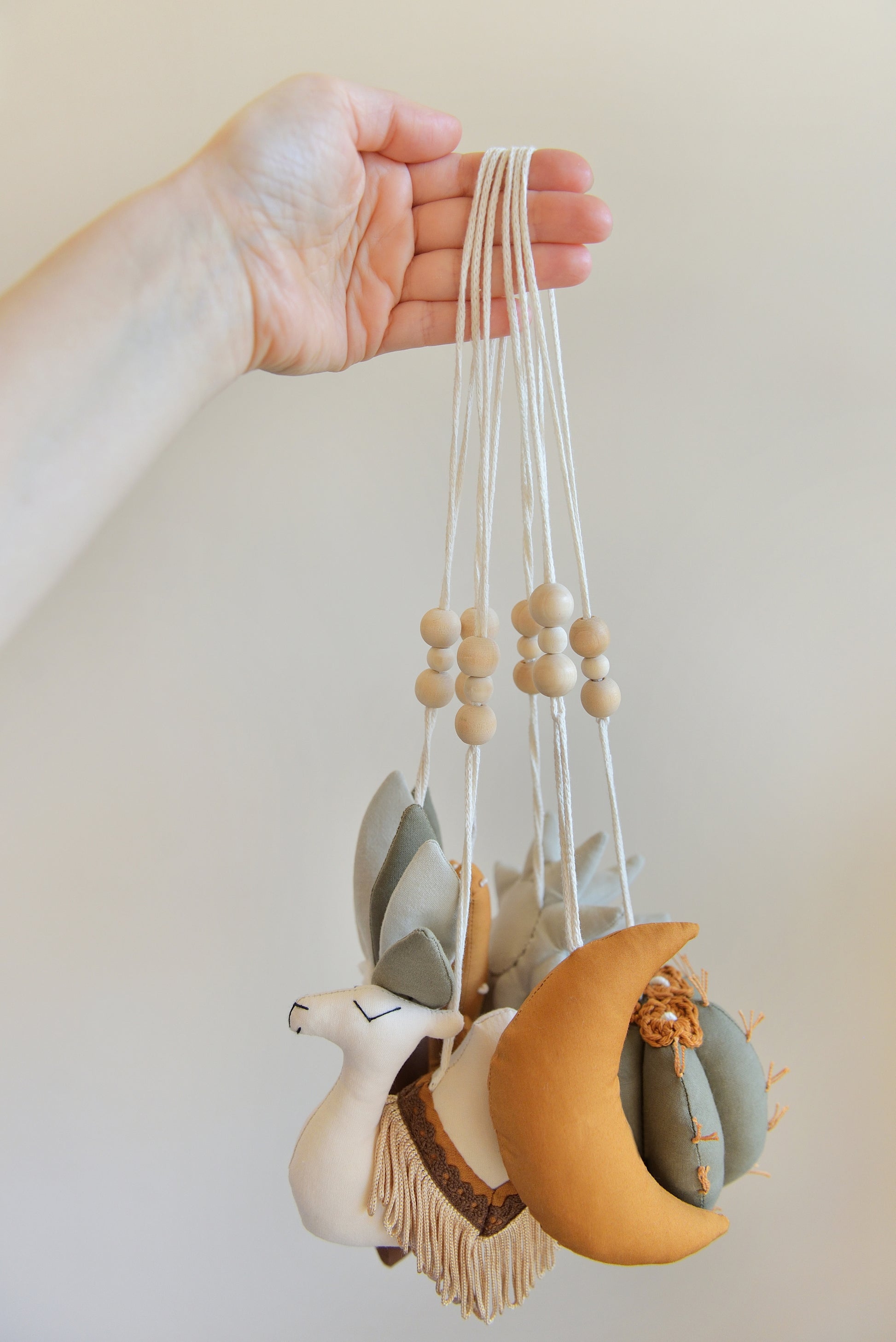 Hand holding desert themed play gym toys: moon, succulent, cacti, palm and camel in khaki, sage, brown and ochre colours.