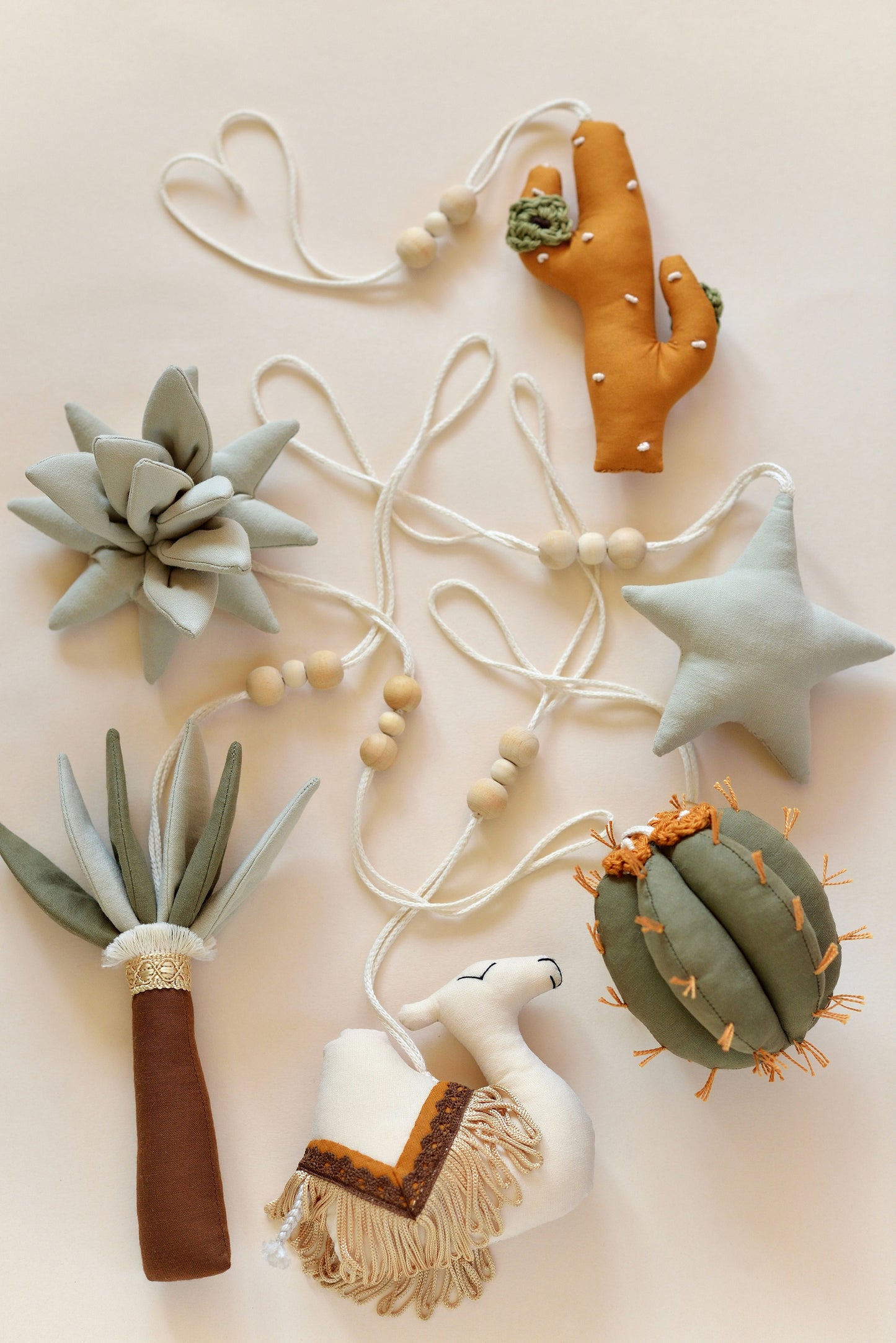 Flatlay of desert themed play gym toys: star, succulent, cacti, palm and camel in khaki, sage, brown and ochre colours.