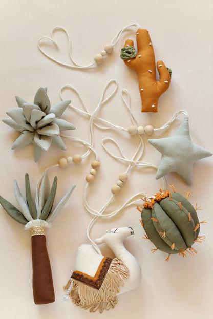 Flatlay of desert themed play gym toys: star, succulent, cacti, palm and camel in khaki, sage, brown and ochre colours.