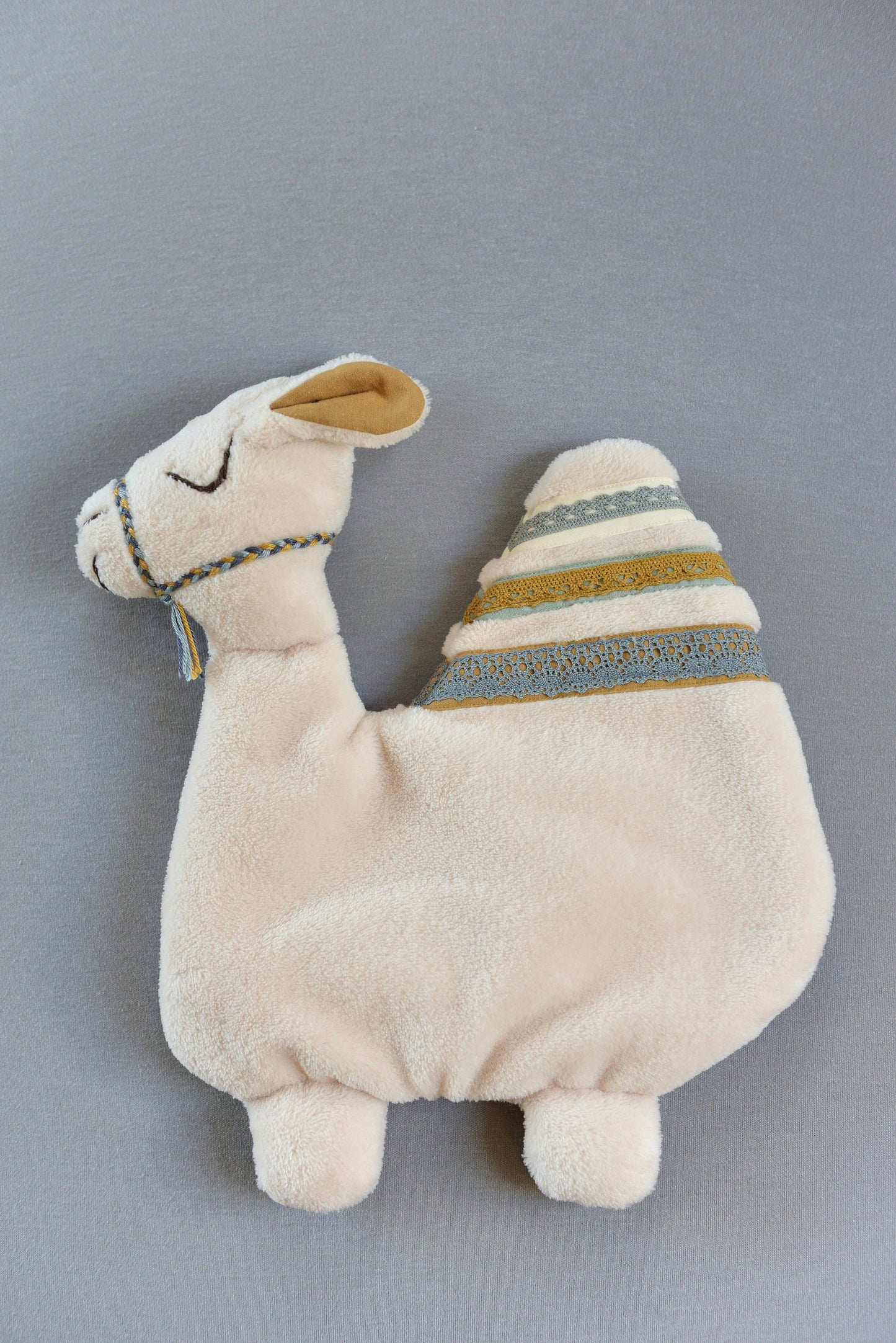 Handmade camel shaped baby comforter with ivory body and mustard, blue lace details on a blue background.