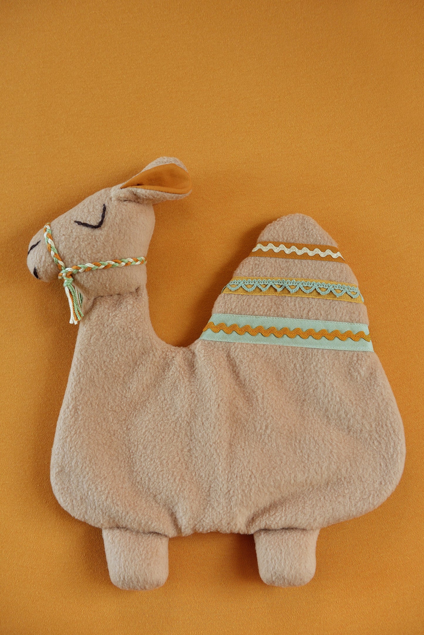 Handmade camel shaped baby comforter with tan body and green, tan and rust  lace details on a rust background.
