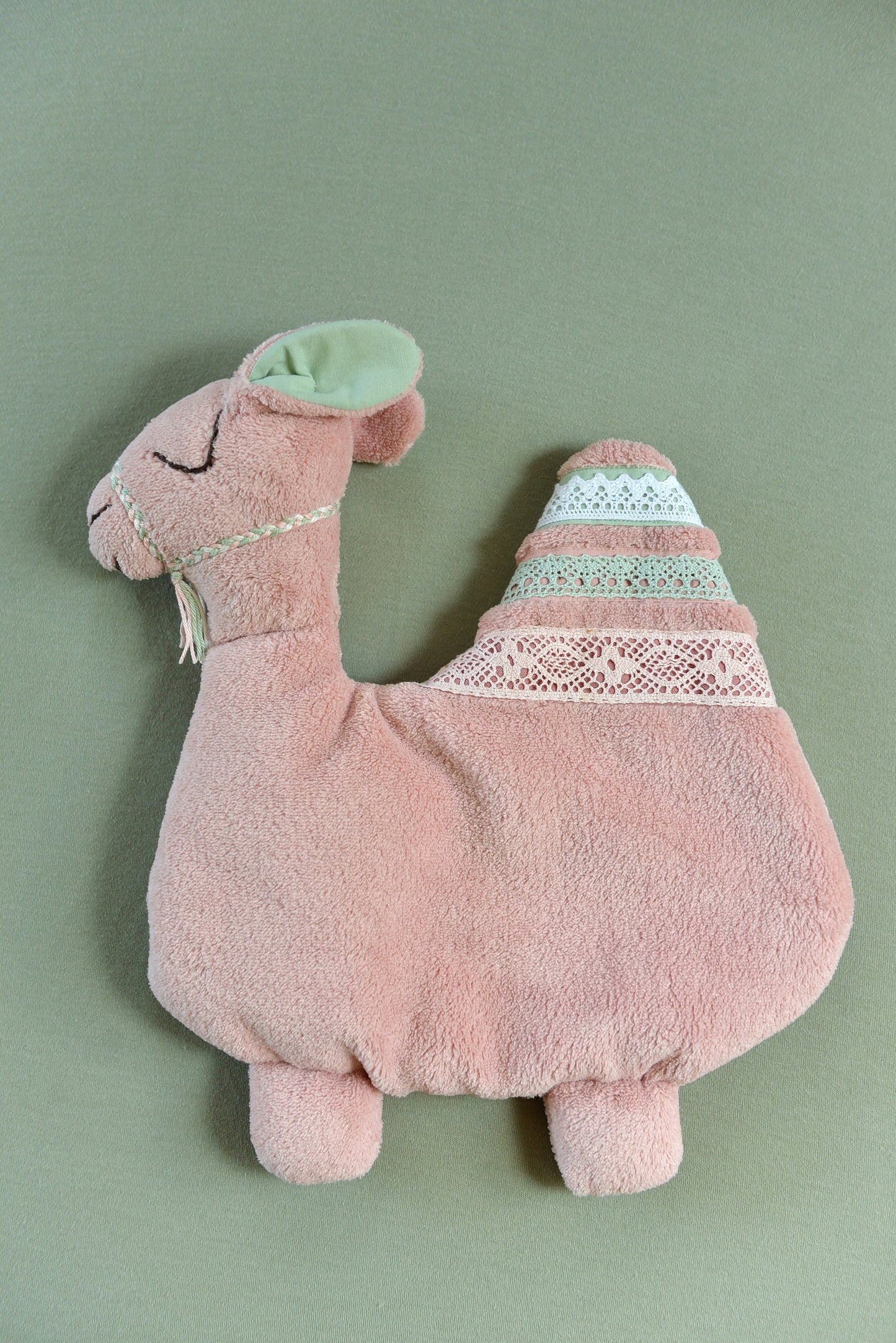 Handmade camel shaped baby comforter with blush pink body and white, pastel pink and mint green lace details on a dark mint background.