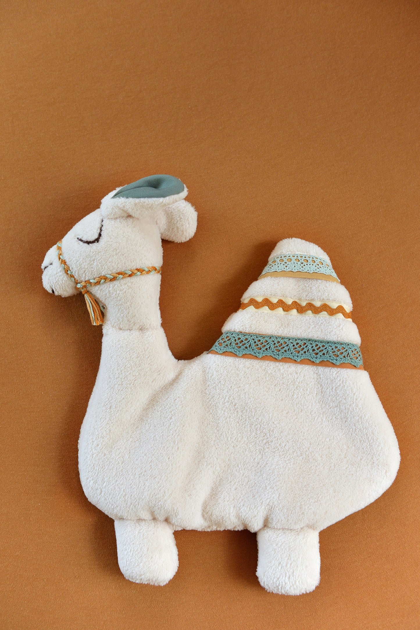 Handmade camel shaped baby comforter with ivory body and teal, ivory and rust lace details on a brown background.