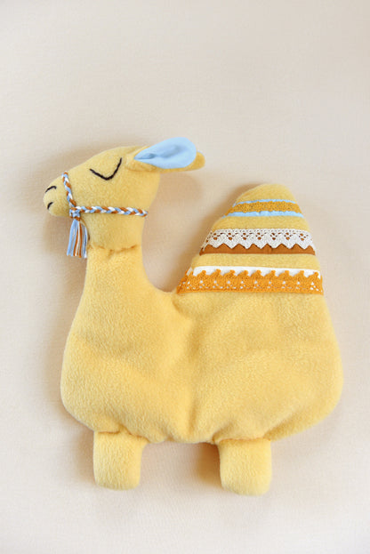 Handmade camel shaped baby comforter with pastel yellow body and white, marigold, blue and rust lace details on an ivory background.
