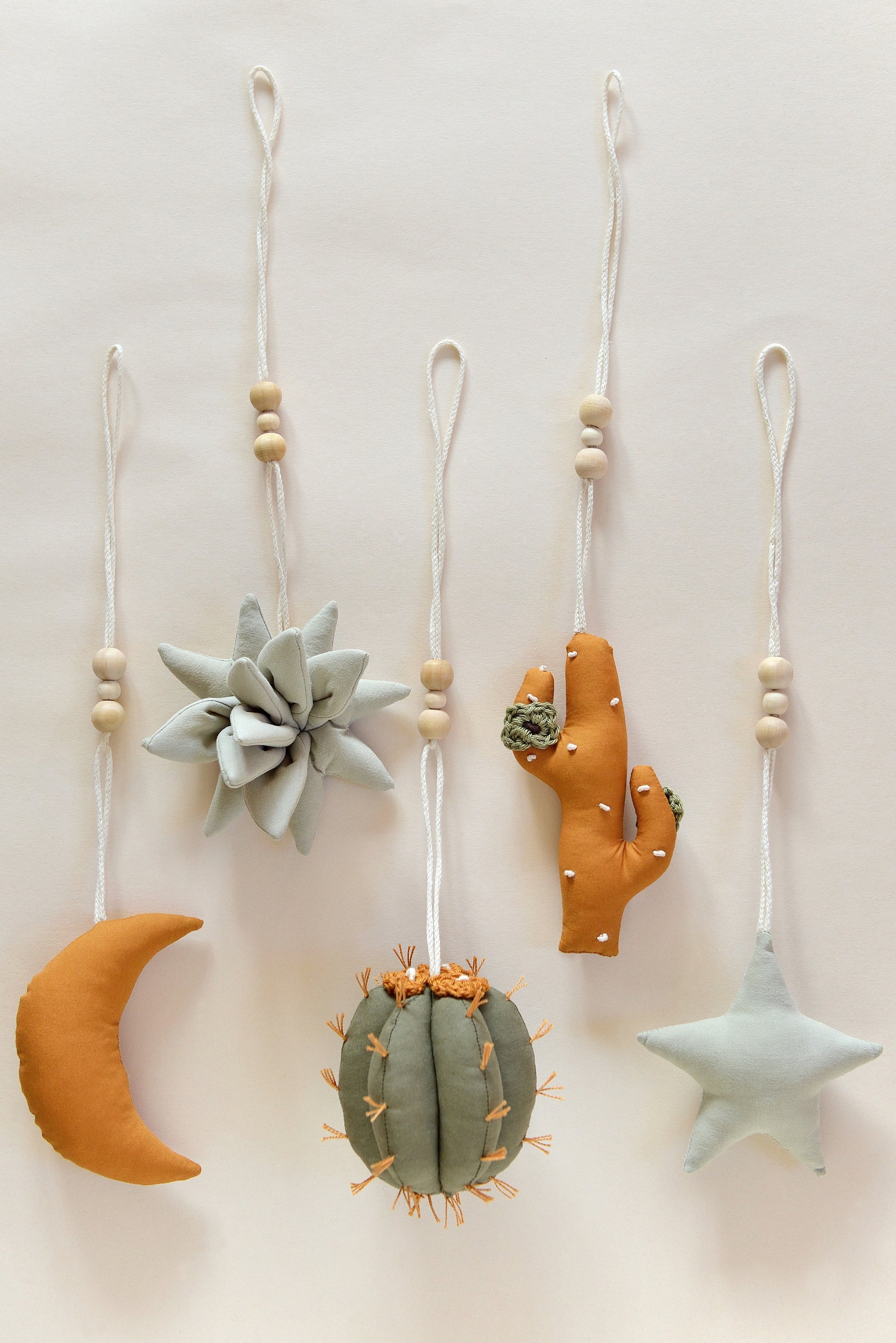 Flatlay of desert themed play gym toys: moon, succulent, cacti and star in khaki, sage and ochre colours.