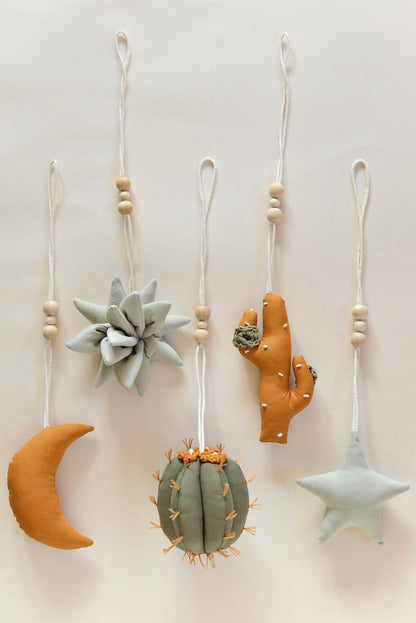 Flatlay of desert themed play gym toys: moon, succulent, cacti and star in khaki, sage and ochre colours.
