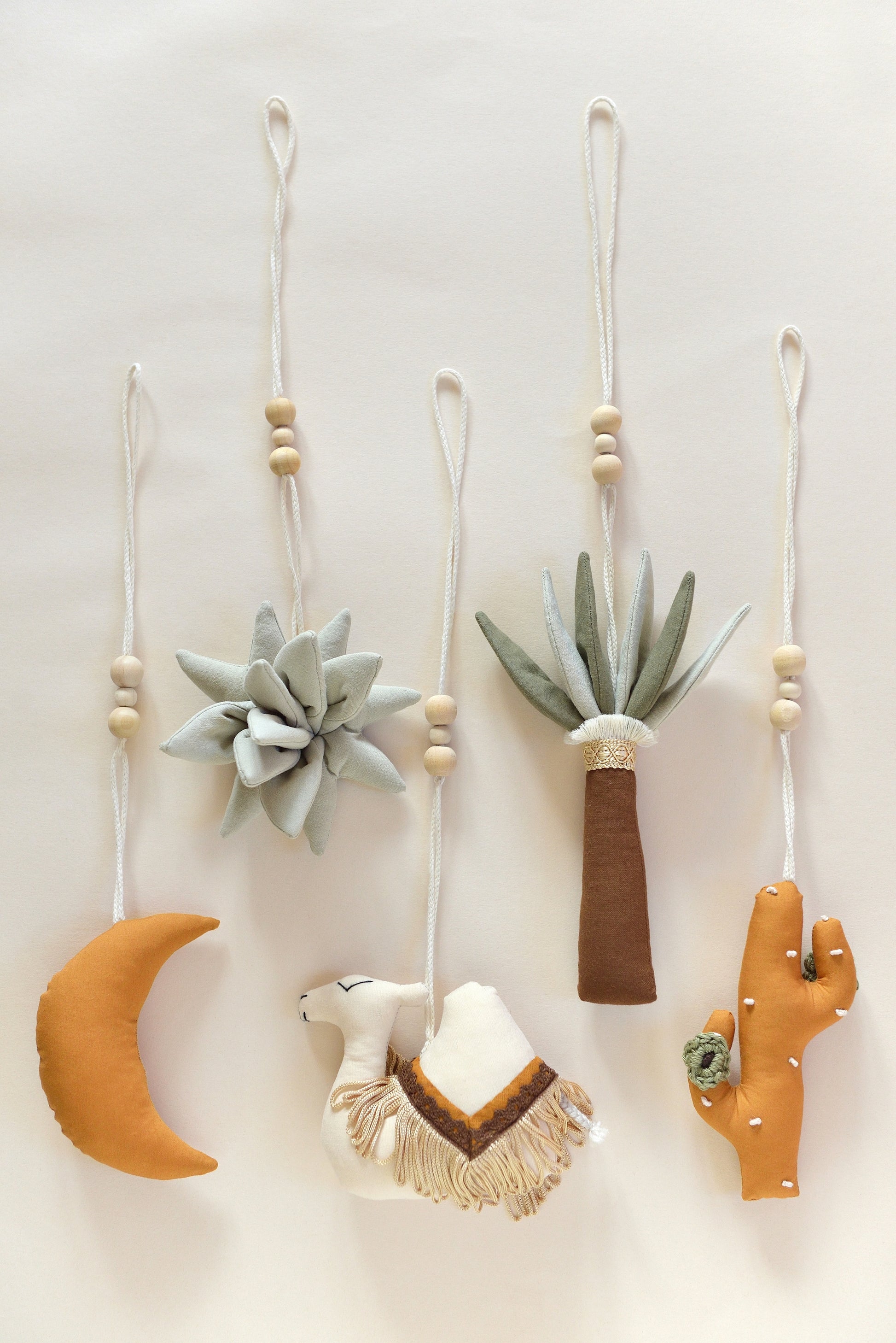 Flatlay of desert themed play gym toys: moon, succulent, cacti, palm and camel in khaki, sage, brown and ochre colours.