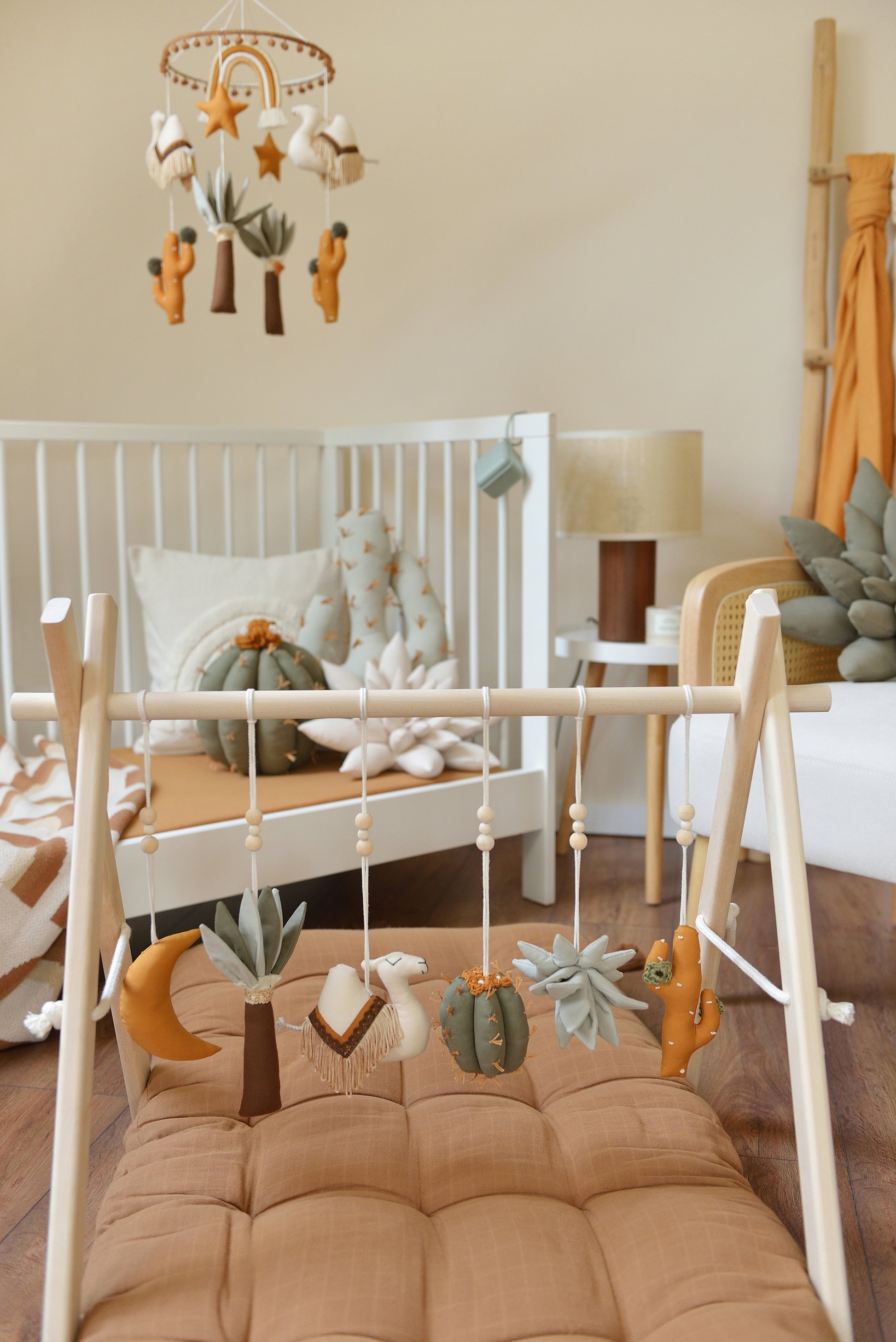 Desert themed baby room with white crib, rattan armchair and baby play gym with hanging toys in the foreground.