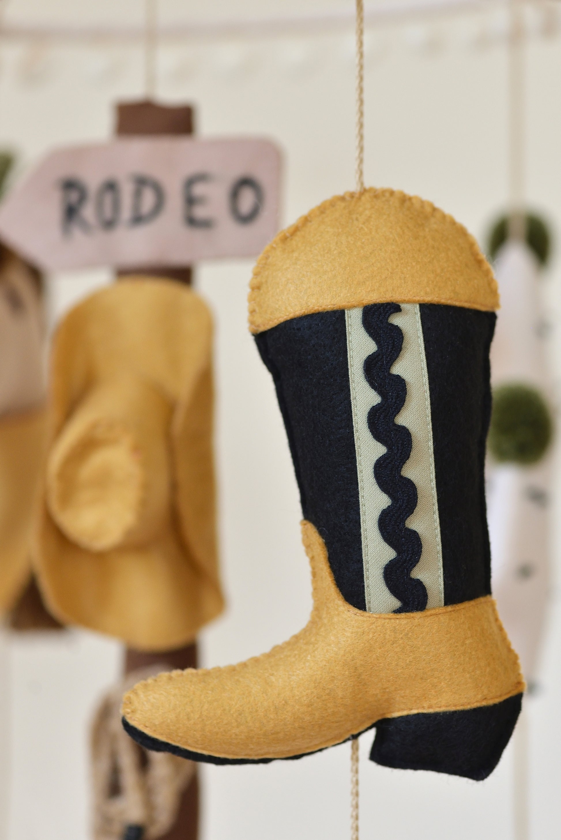 Decorative cowboy boot with wavy pattern hanging on a rope against a rodeo signpost figure with cowboy hat.