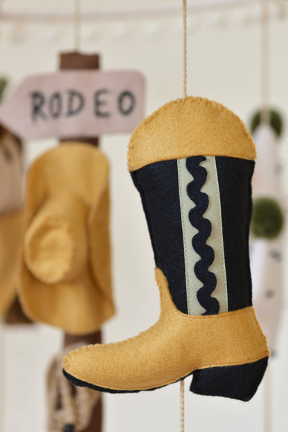 Decorative cowboy boot with wavy pattern hanging on a rope against a rodeo signpost figure with cowboy hat.