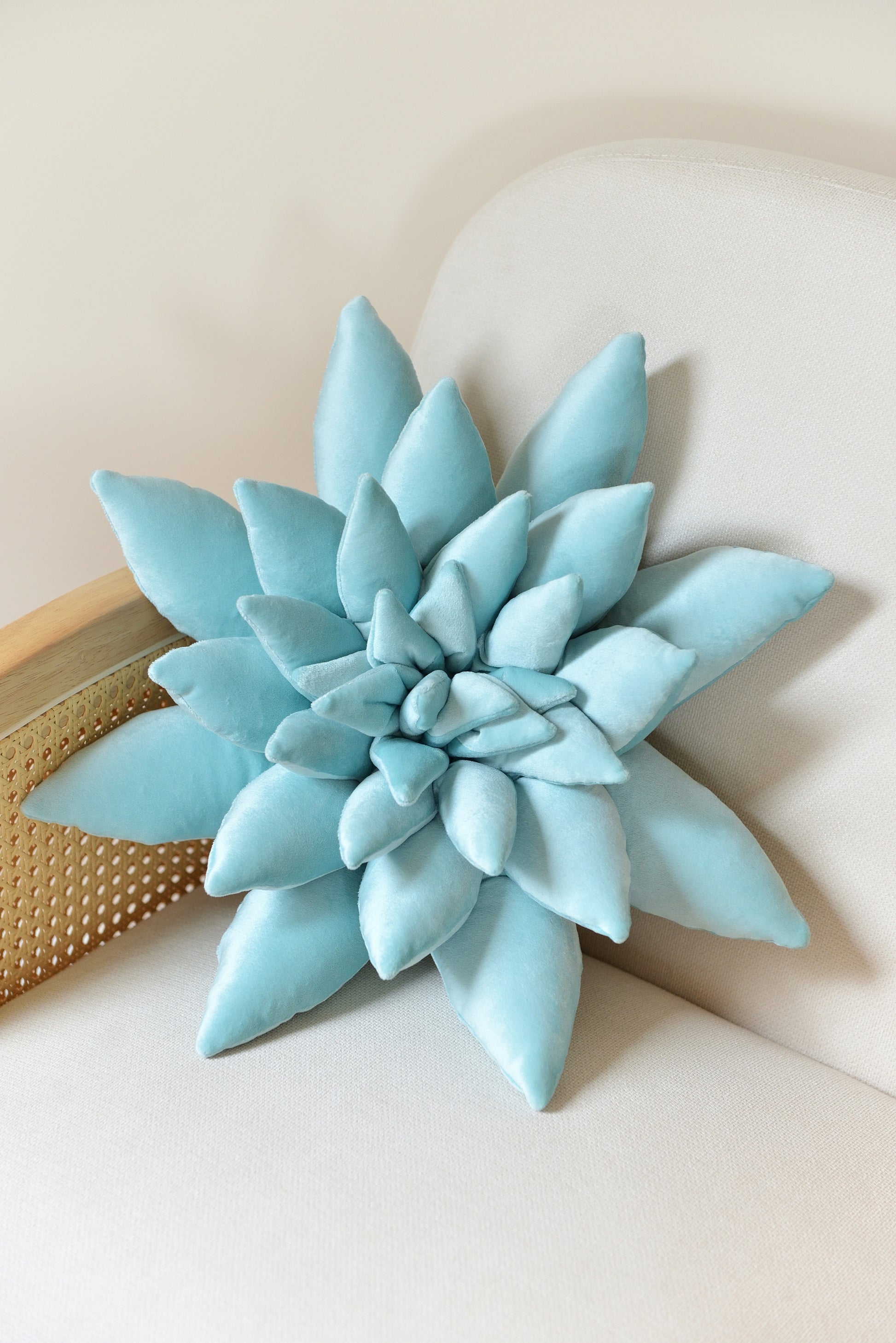 Large succulent shaped velvet decor pillow in aqua blue colour placed on an ivory rattan armchair.