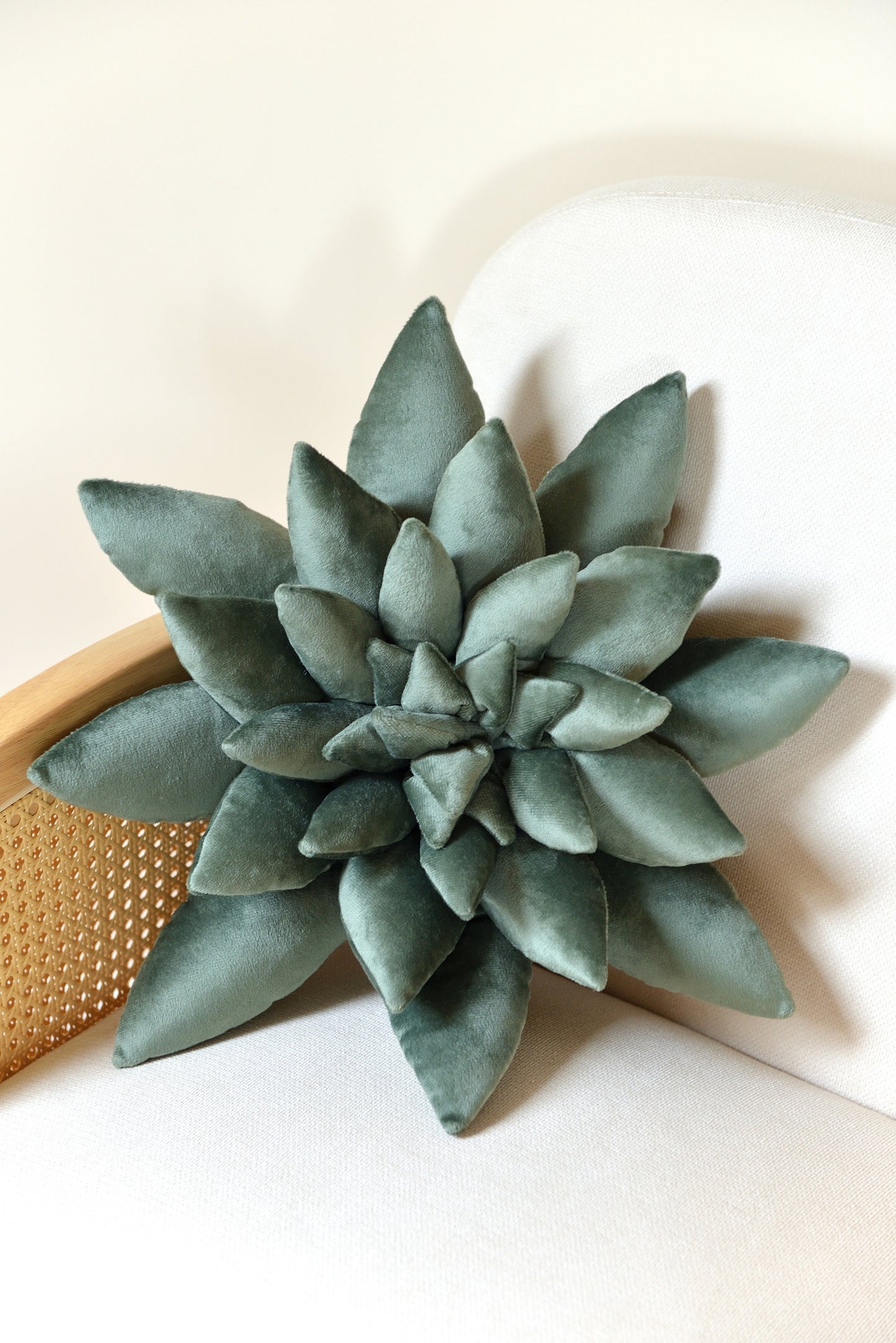 Large succulent shaped velvet decor pillow in jade green colour placed on an ivory rattan armchair.