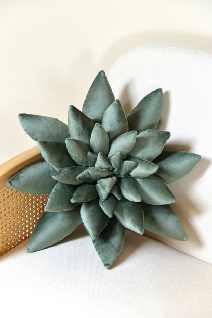 Large succulent shaped velvet decor pillow in jade green colour placed on an ivory rattan armchair.