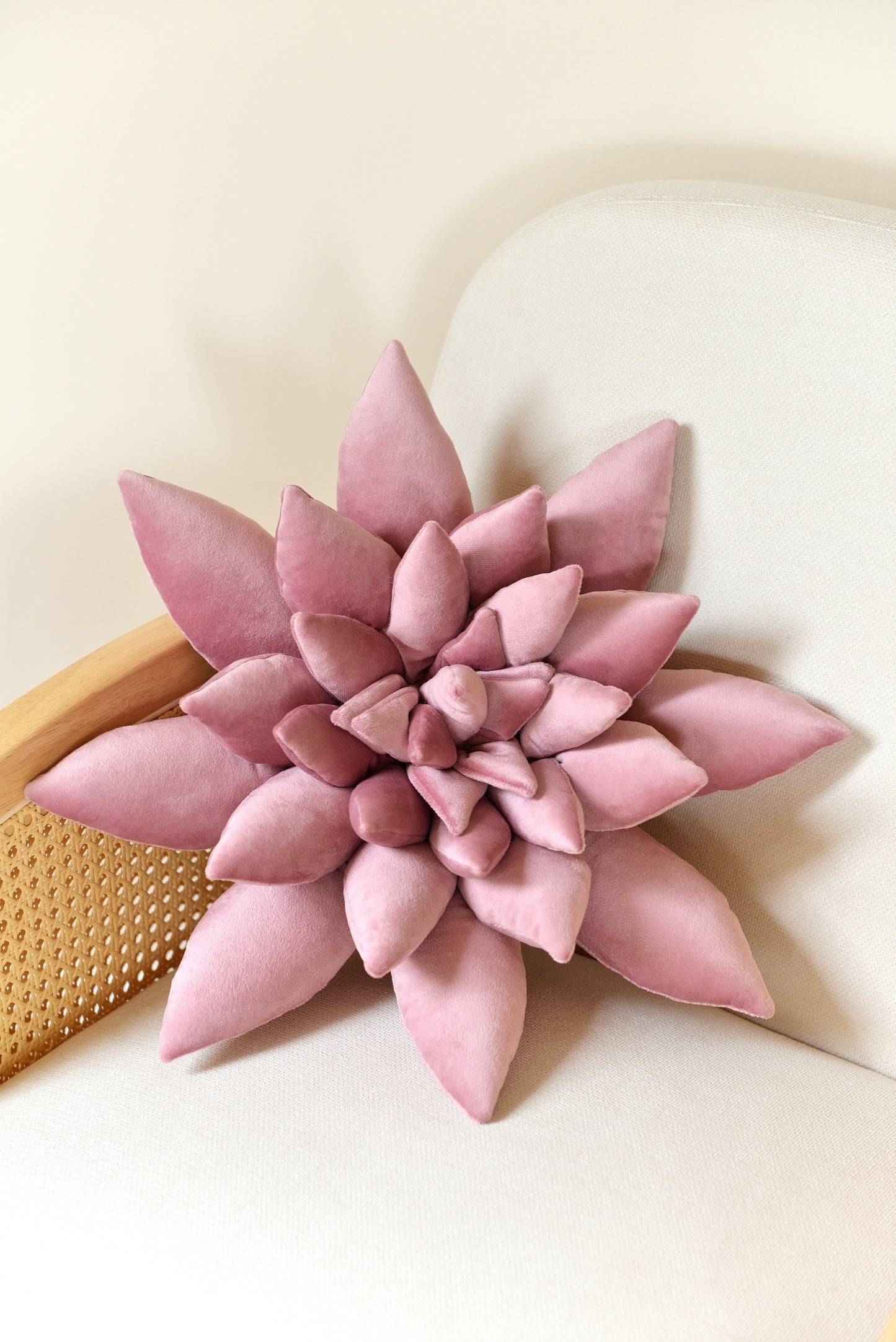 Large succulent shaped velvet decor pillow in lilac colour placed on an ivory rattan armchair.