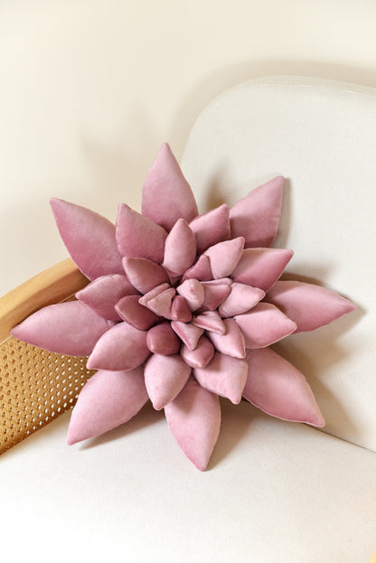 Large succulent shaped velvet decor pillow in lilac colour placed on an ivory rattan armchair.