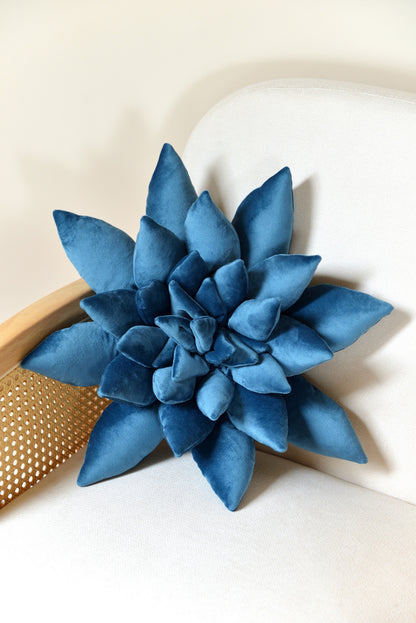 Large succulent shaped velvet decor pillow in ocean blue colour placed on an ivory rattan armchair.