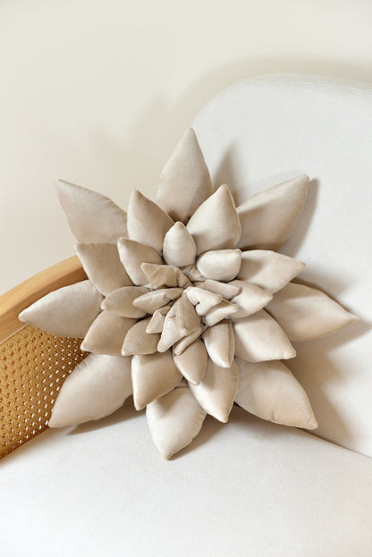 Large succulent shaped velvet decor pillow in pearl colour placed on an ivory rattan armchair.