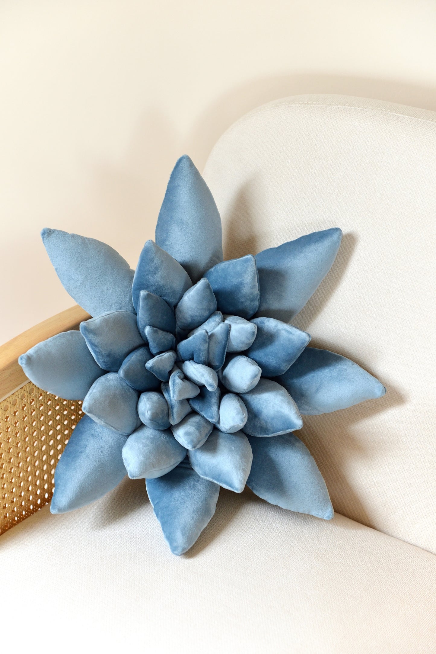 Large succulent shaped velvet decor pillow in sky blue colour placed on an ivory rattan armchair.